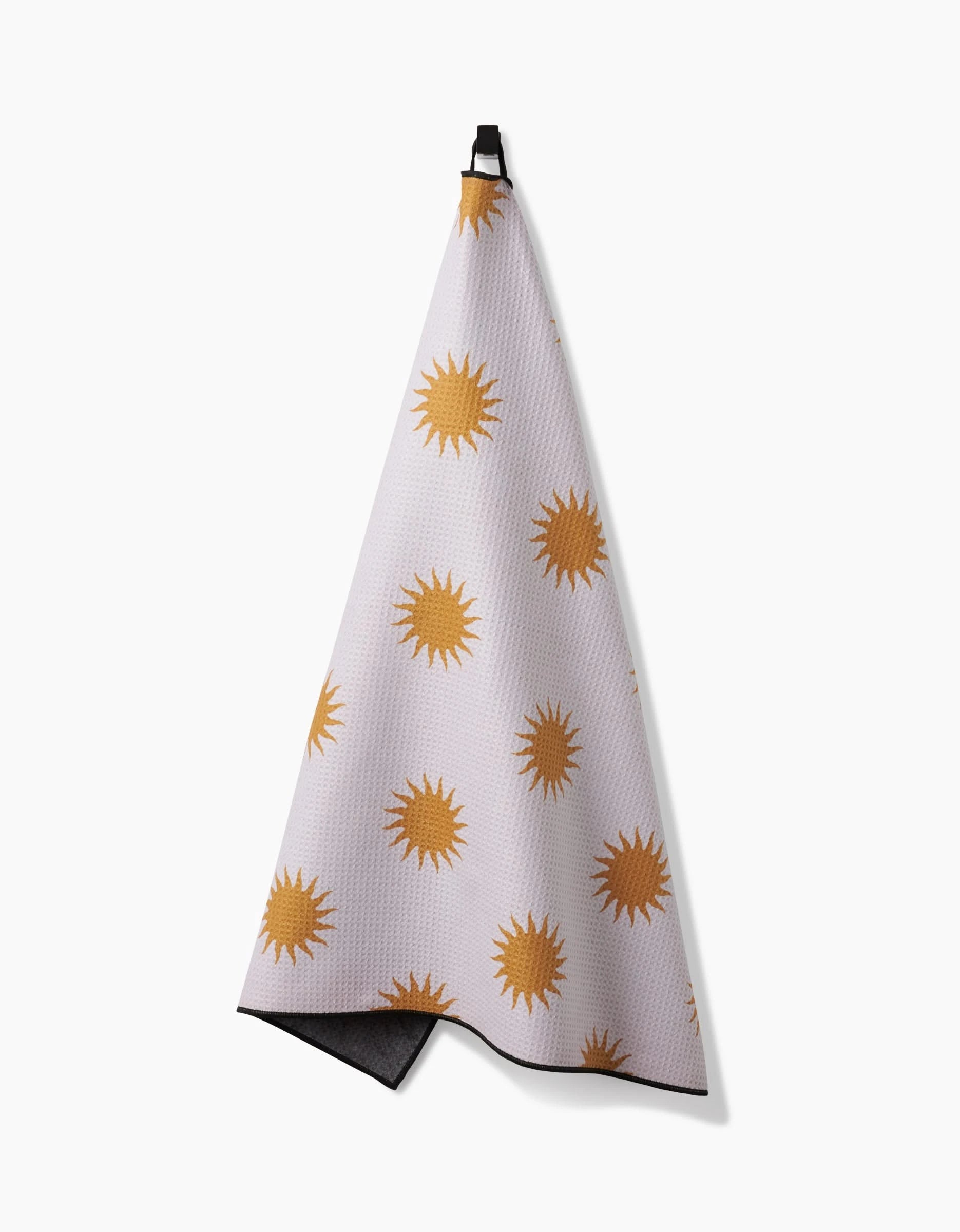 The Geometry Feeling Sunny towel, featuring golden yellow sun shapes on white, hangs from a black loop for easy drying—making it a quick-dry, practical choice for your bath or as a dog towel.