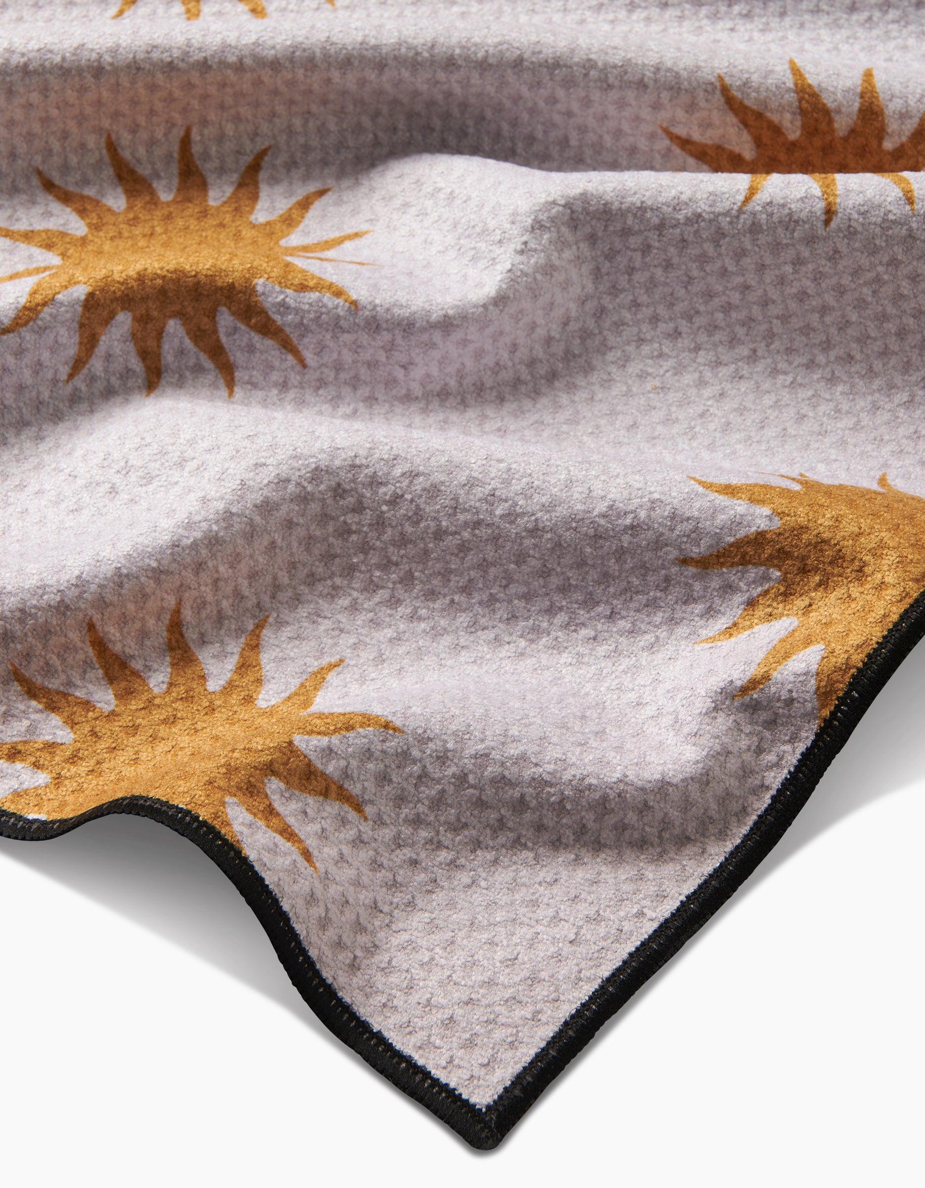 A close-up of Geometry’s Feeling Sunny dog towel shows its textured light gray fabric, large golden-yellow suns with radiating rays, black trim, and gentle folds. This highly absorbent, quick-drying blanket is perfect for your pet.