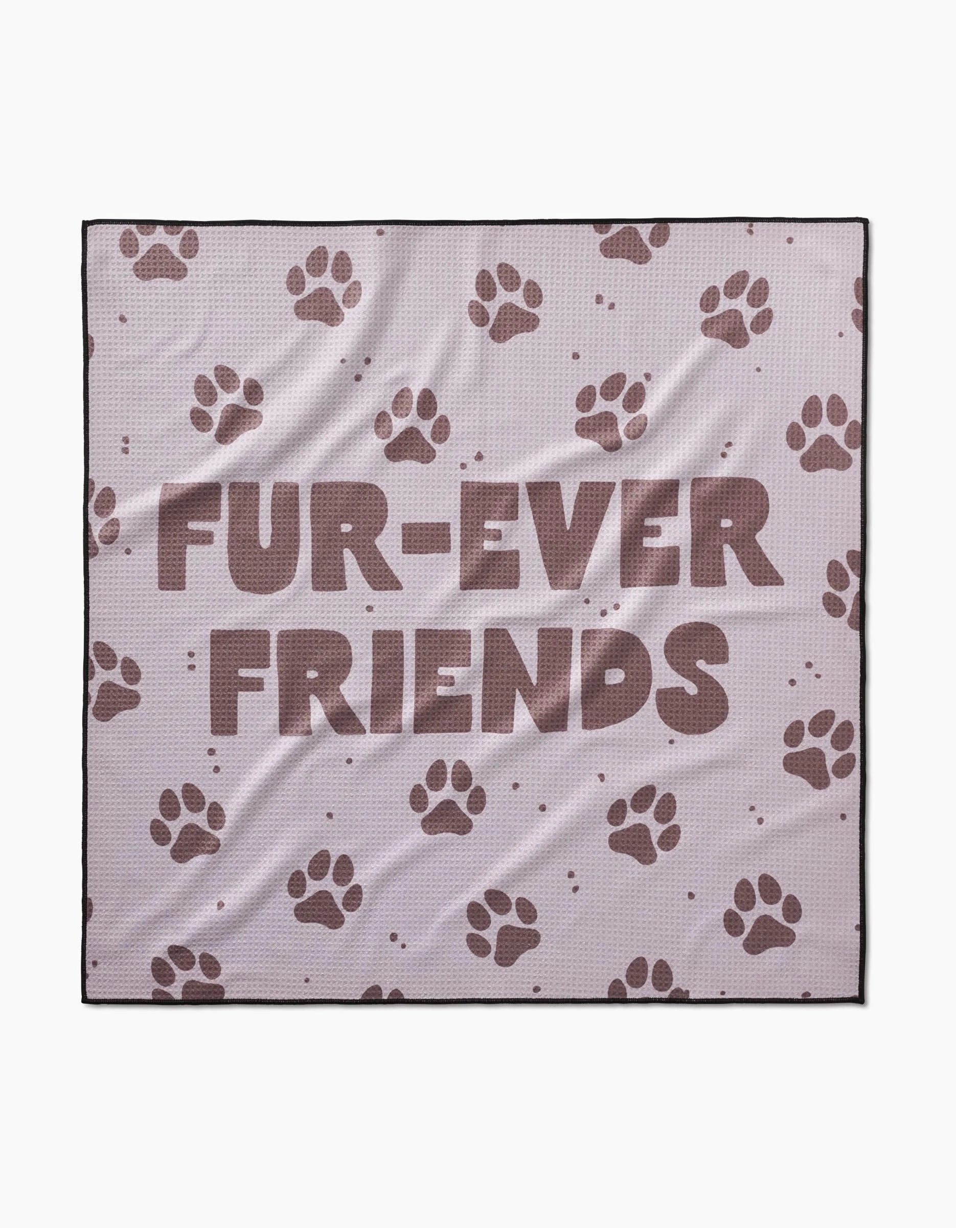 The Geometry Fur Ever Friends blanket is light purple, crafted from recycled materials, and decorated with brown paw prints plus “FUR-EVER FRIENDS” in bold letters.