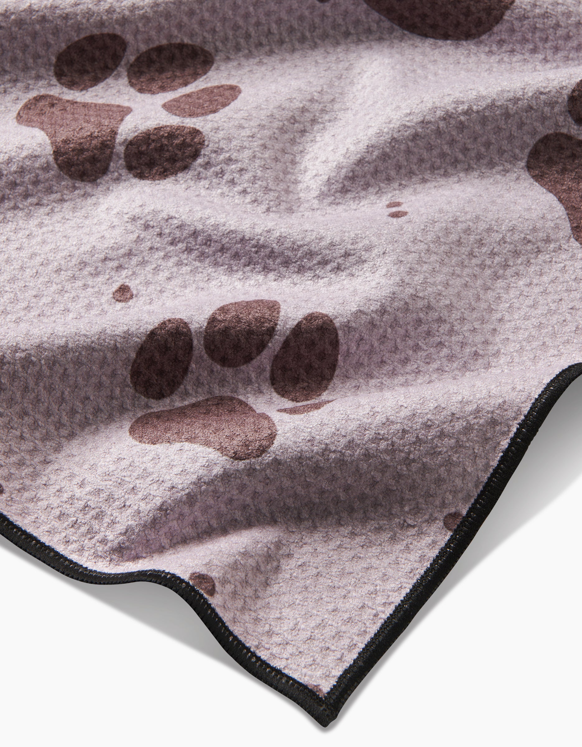 The Geometry Fur Ever Friends blanket is light purple with a textured surface, dark brown paw prints, and black trim. Made from recycled materials, it features gentle folds and creases for a cozy look.