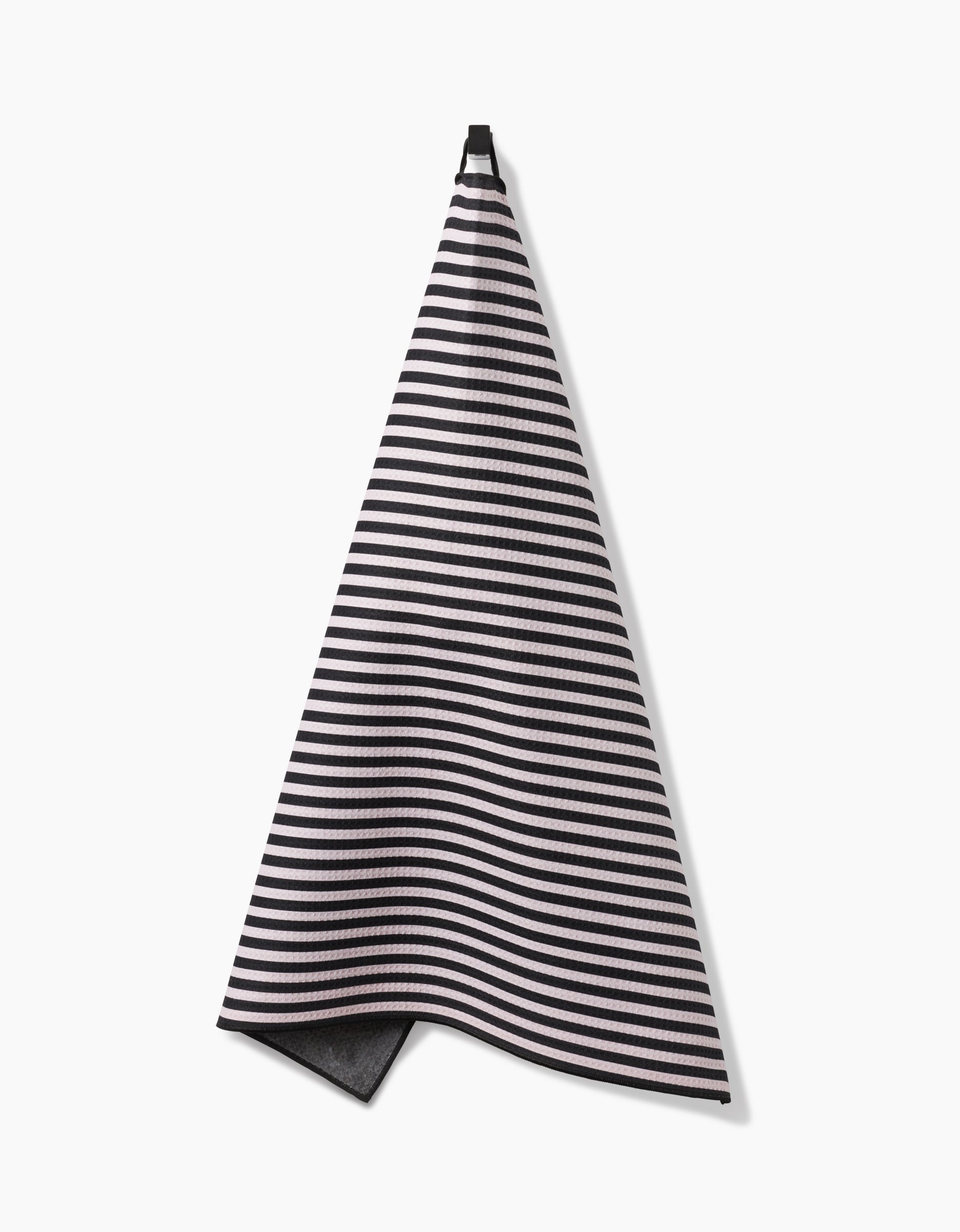 The Geometry Good Pup towel, featuring black and white stripes and made from recycled materials, hangs from a hook against a plain white background.