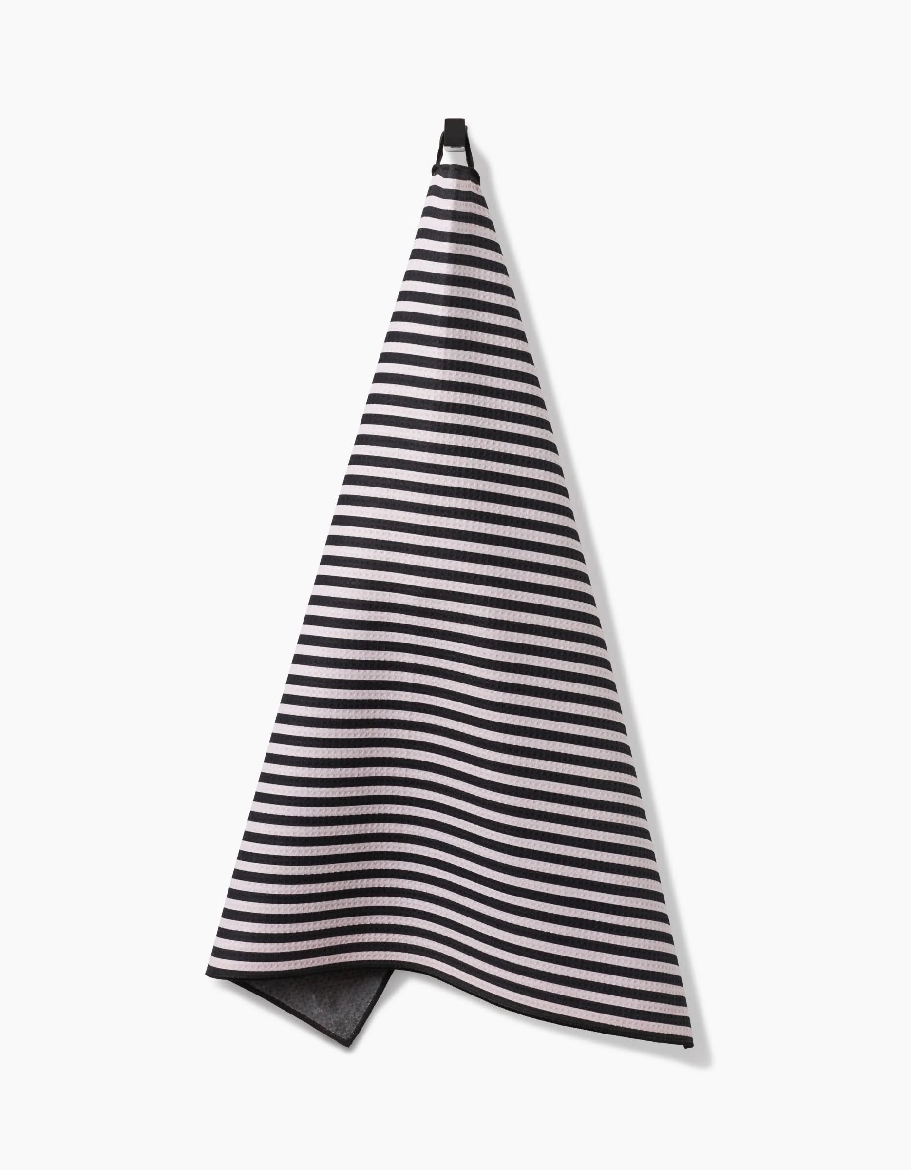 The Geometry Good Pup towel, featuring black and white stripes and made from recycled materials, hangs from a hook against a plain white background.