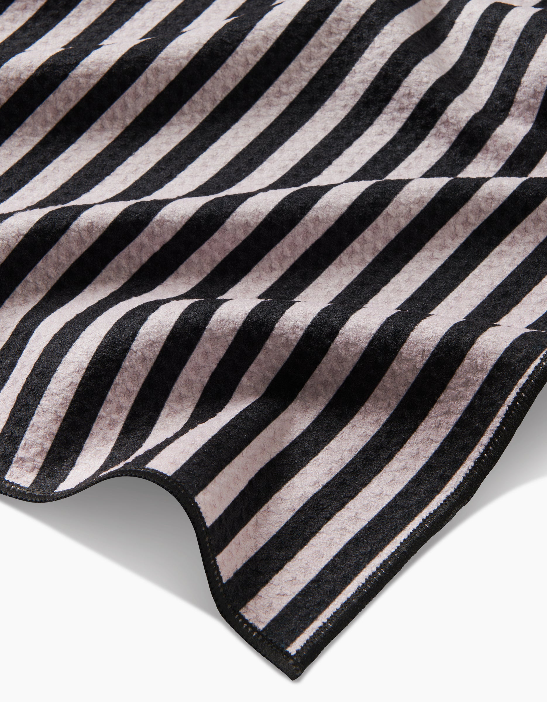 A close-up of Geometrys Good Pup towel, made from recycled materials, shows soft, highly absorbent fabric with diagonal black and light gray stripes. Slightly curled edges reveal its texture and thickness—ideal for drying your dog.