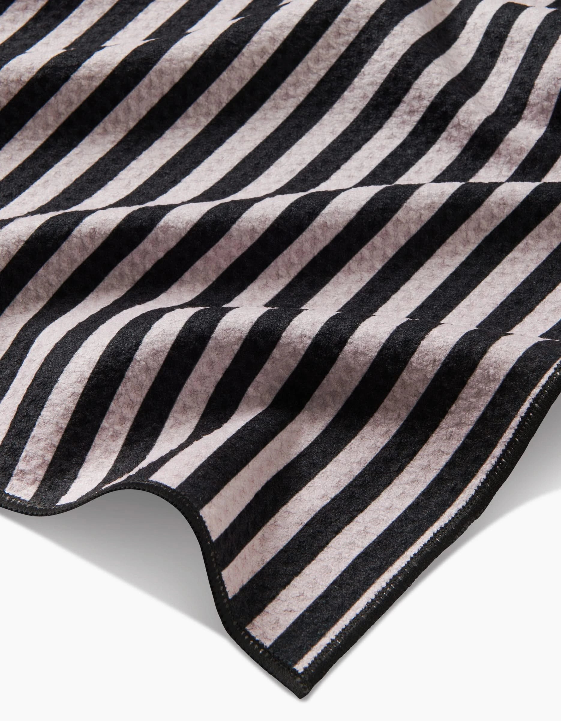 A close-up of Geometrys Good Pup towel, made from recycled materials, shows soft, highly absorbent fabric with diagonal black and light gray stripes. Slightly curled edges reveal its texture and thickness—ideal for drying your dog.
