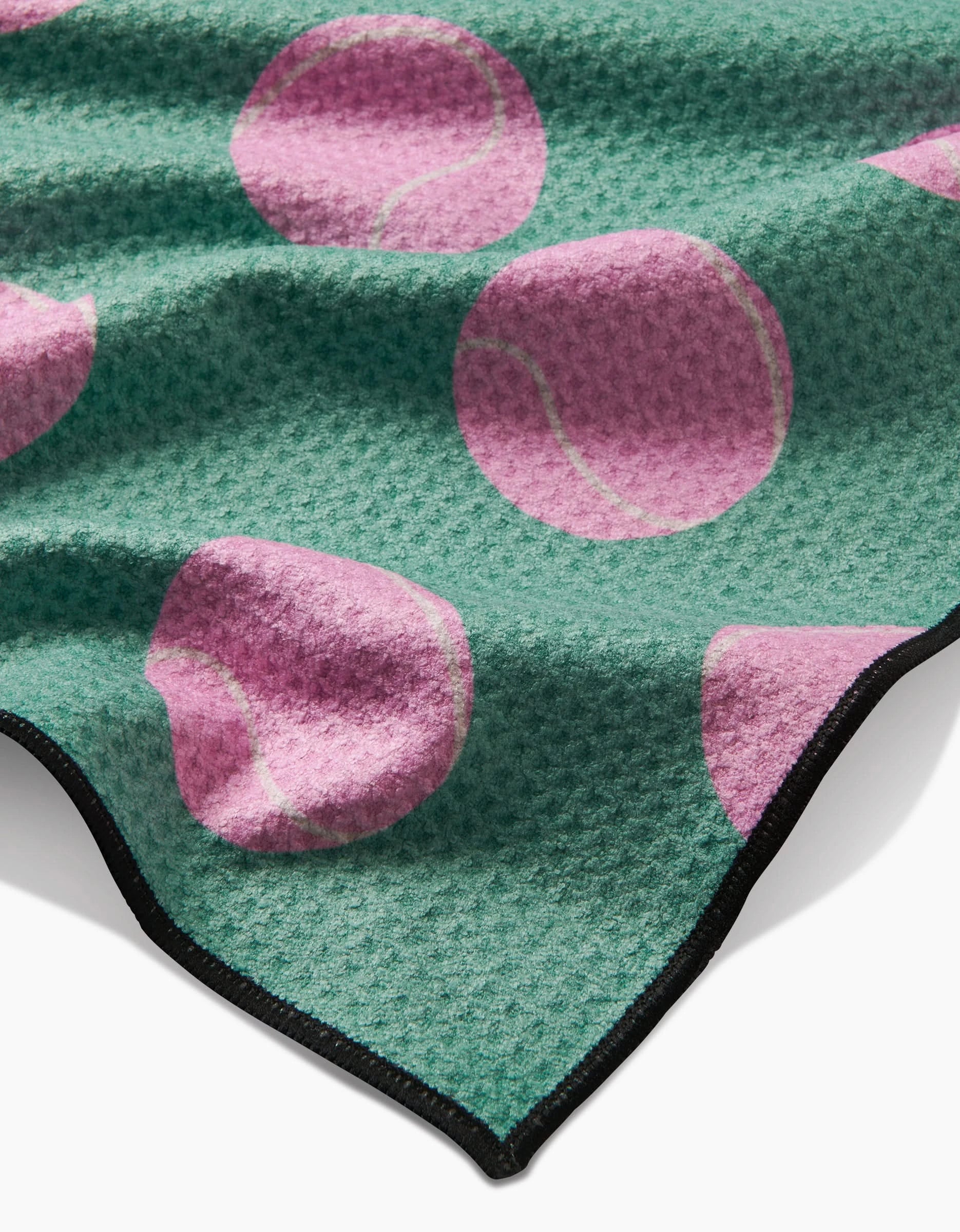 The Geometry Pink Ball is a green textured dog towel made from recycled materials, featuring large pink tennis ball patterns and a black edge trim.