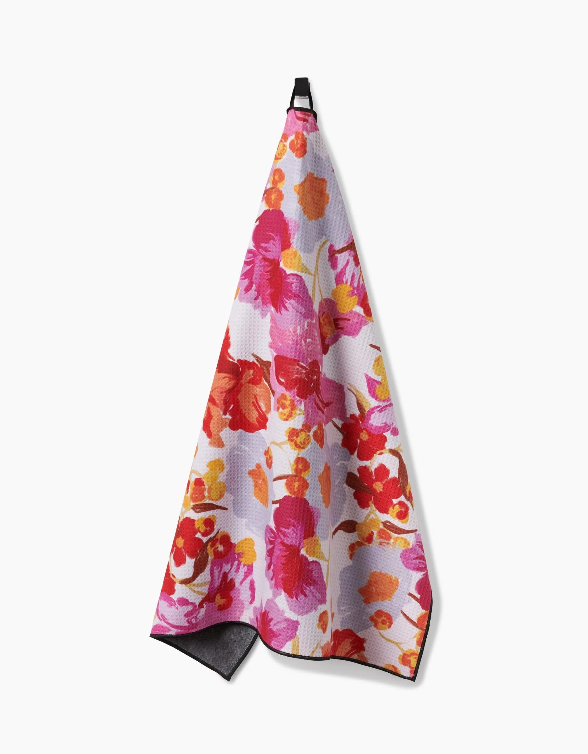 The Geometry Pup Florals towel features a colorful floral pattern in pink, red, orange, and yellow shades and hangs from a black loop against a white background. Highly absorbent and stylish, its perfect for brightening up any space.