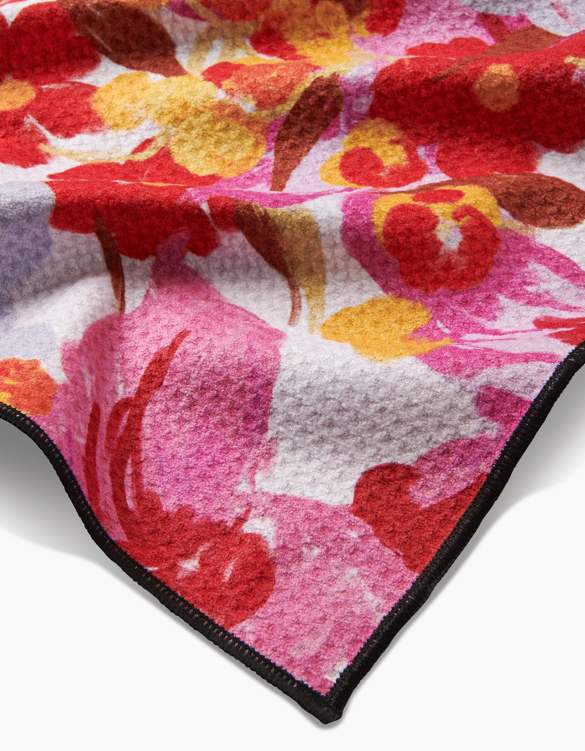 A close-up of the Geometry Pup Florals blanket, featuring a vibrant red, pink, yellow, and orange floral pattern on soft, highly absorbent recycled material with a black stitched edge visible in the corner.
