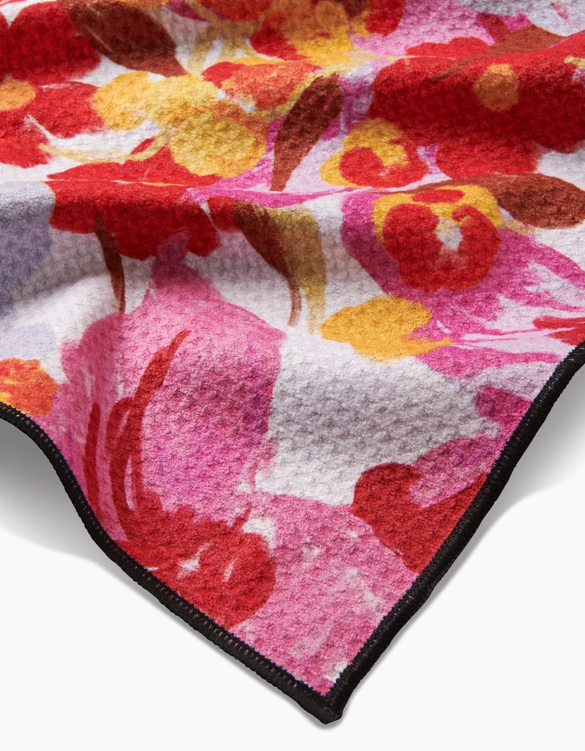 A close-up of the Geometry Pup Florals blanket, featuring a vibrant red, pink, yellow, and orange floral pattern on soft, highly absorbent recycled material with a black stitched edge visible in the corner.