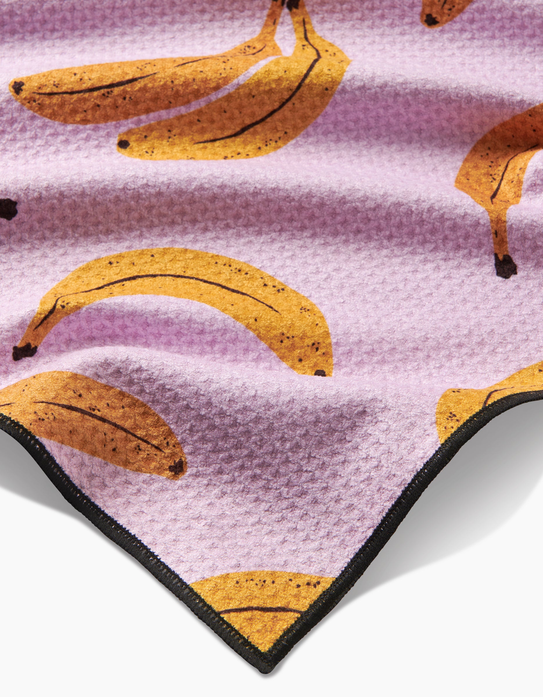A close-up of Geometry’s Pupnana Dog Towel, a highly absorbent light purple fabric with a yellow banana pattern and black trim.