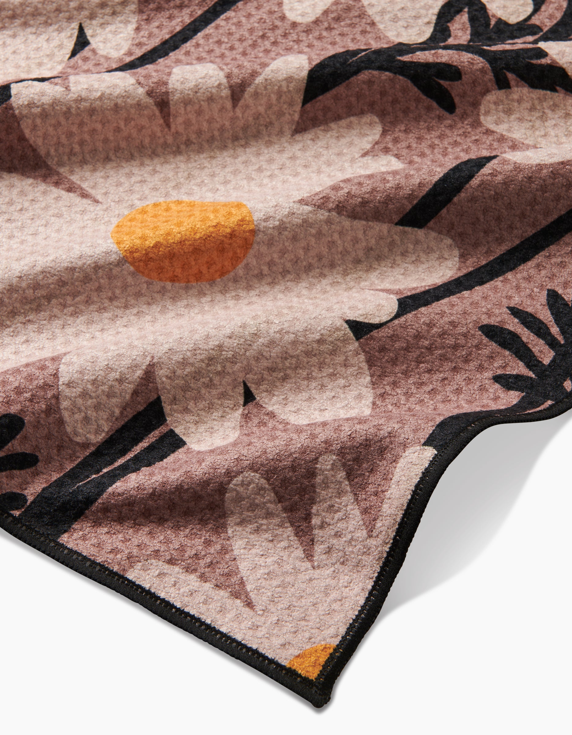 A close-up of Geometry’s Sweet Daisies blanket, crafted from recycled materials, shows large white daisies with yellow centers and black stems on a muted pink background, finished with a black stitched edge.