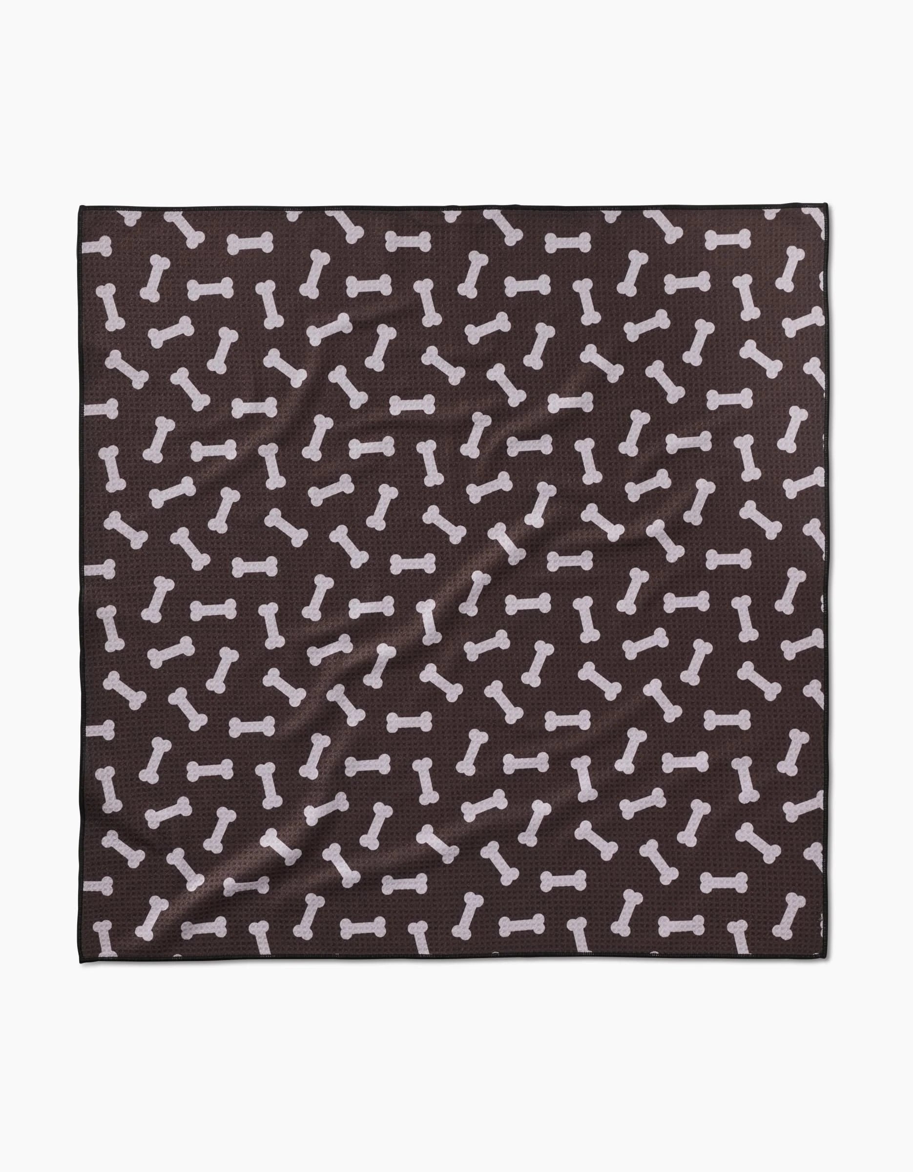 The Geometry Sweet Treats is a black square cloth made from recycled materials, decorated with a pattern of white dog bones scattered across its surface.