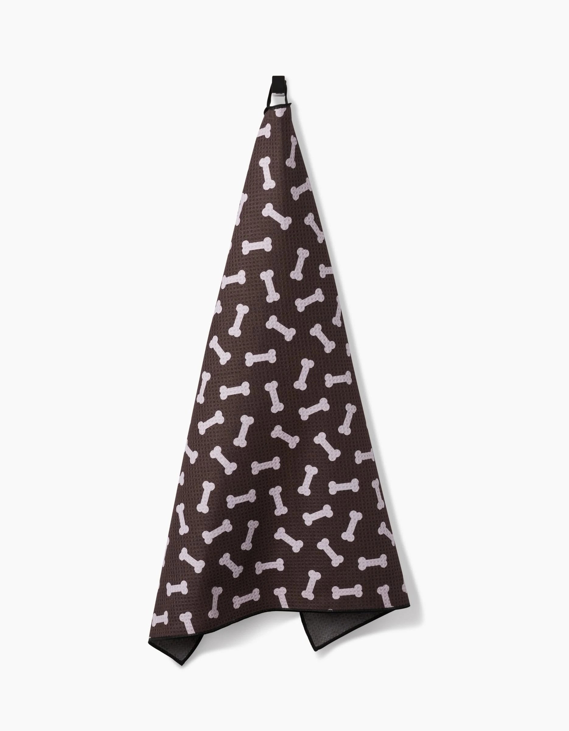 The Geometry Sweet Treats towel, made from highly absorbent recycled materials, features a playful dog bone pattern and hangs from a black loop against a white background.