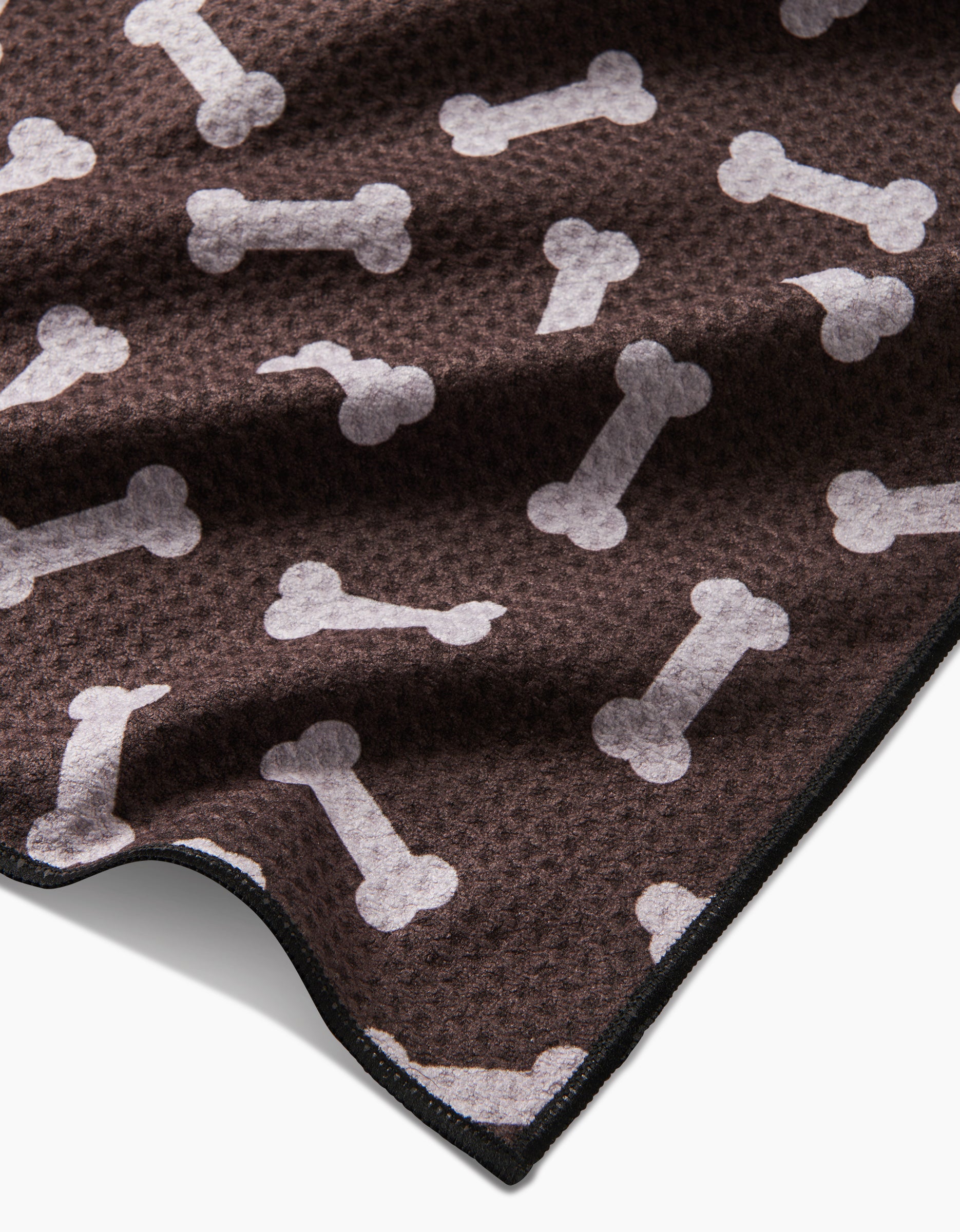 The Geometry Sweet Treats blanket is brown with a white dog bone pattern, textured, eco-friendly from recycled materials, and has a slightly folded corner.