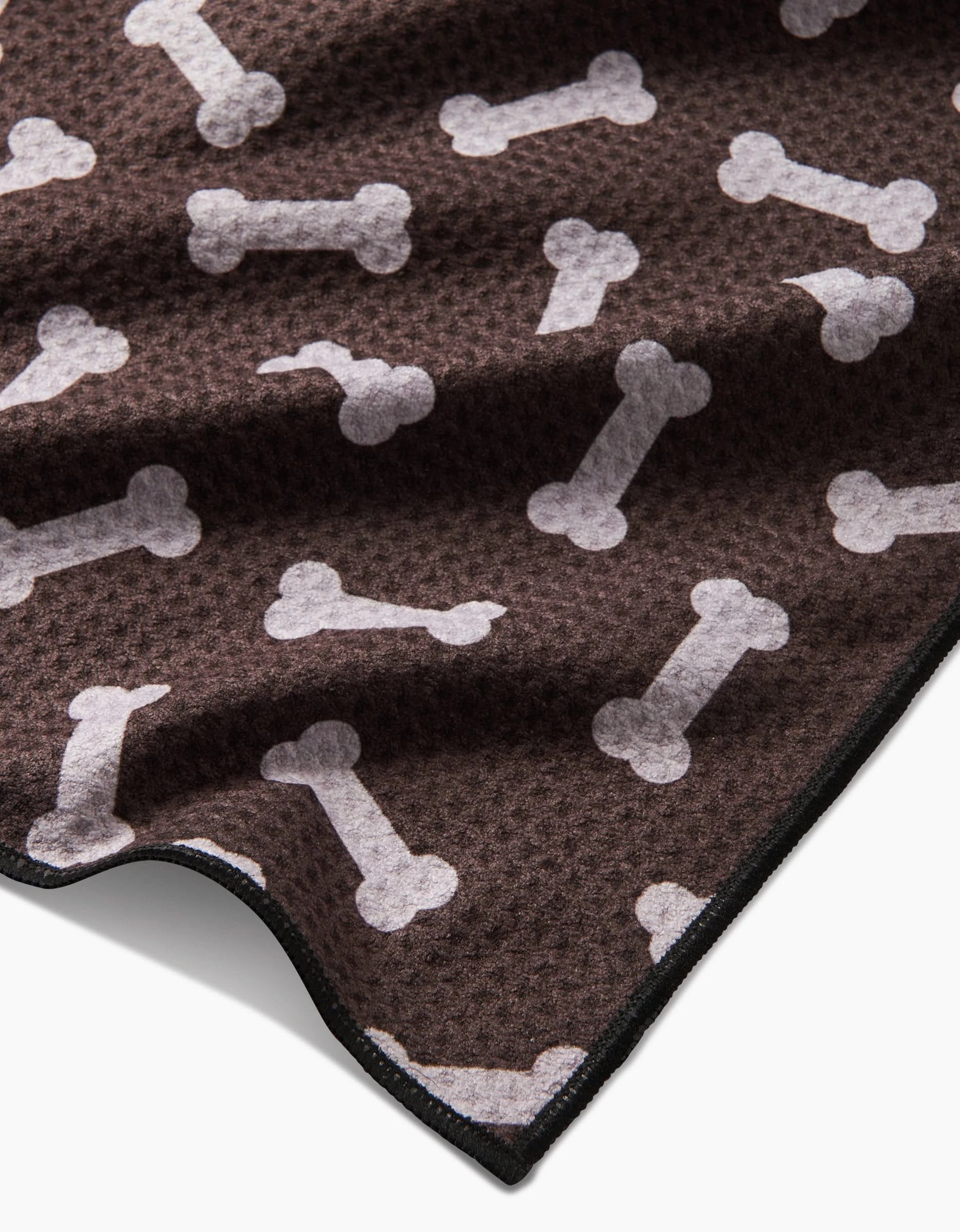 The Geometry Sweet Treats blanket is brown with a white dog bone pattern, textured, eco-friendly from recycled materials, and has a slightly folded corner.