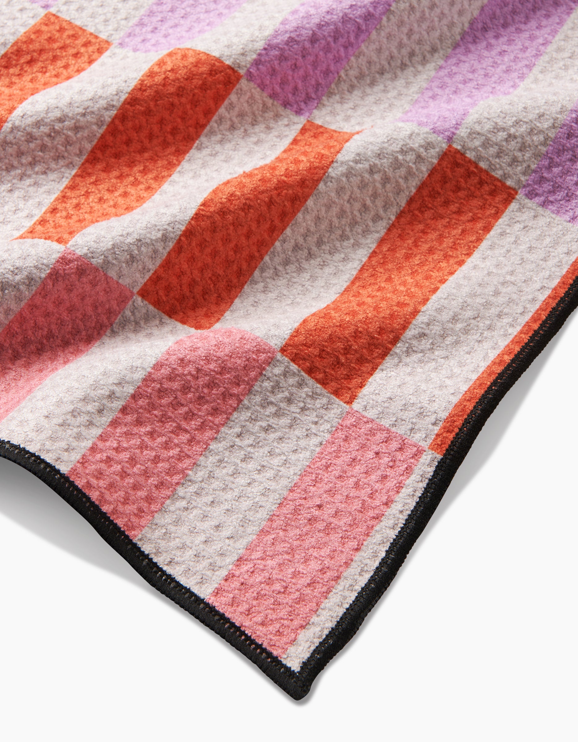 The Geometry Wag Wise blanket features a checkered pattern in pink, red, and lavender squares, crafted from recycled materials with a black stitched border for added detail.