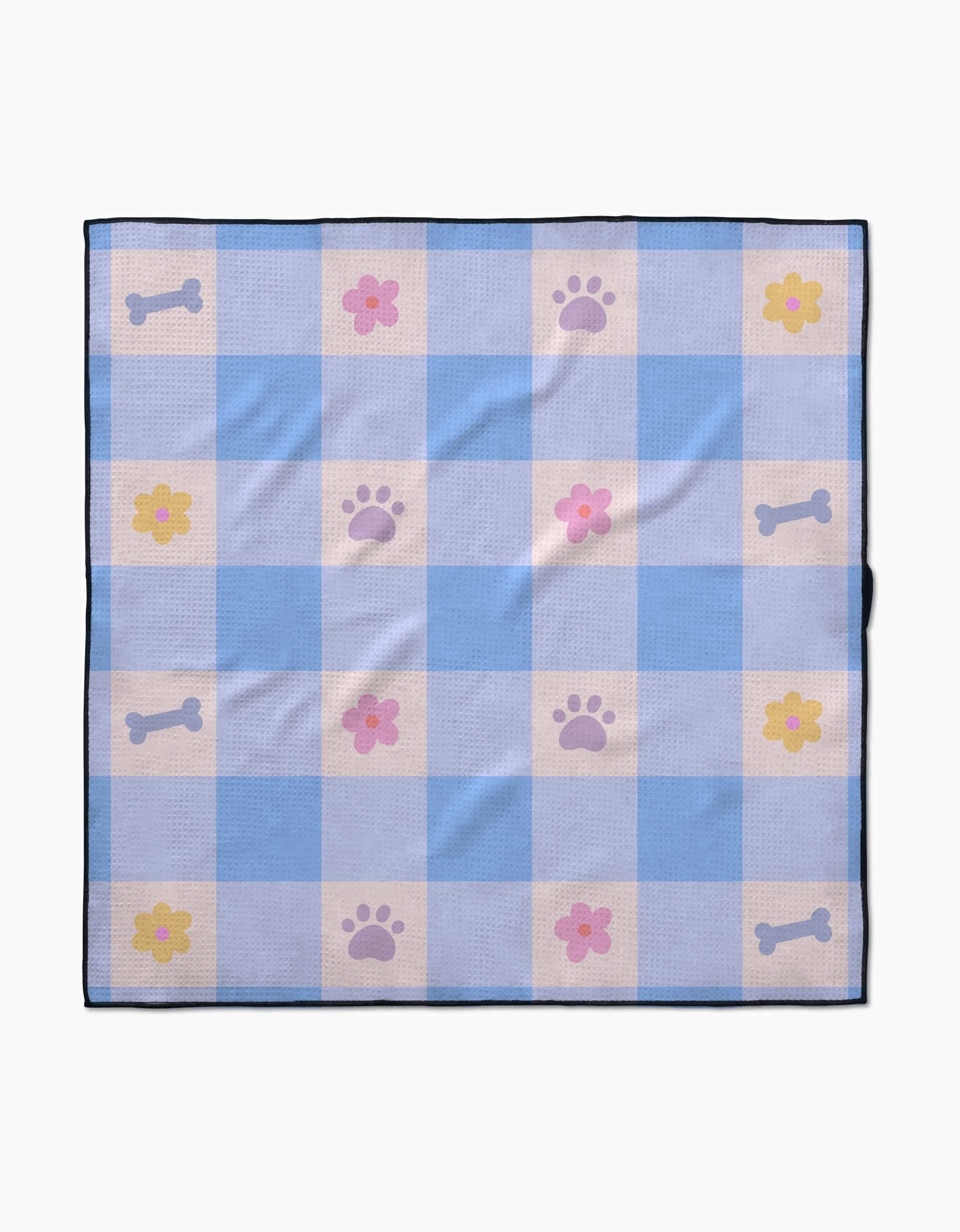 The Blue Sky Picnic Dreams dog towel by Letters By Shells features blue and white checks with pink flowers, purple paw prints, and light gray dog bones. Made from recycled materials, it’s finished with a dark blue border.