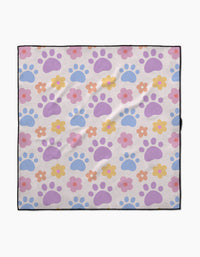 The Paws and Daisies dog towel by Letters By Shells is highly absorbent, made from recycled materials, and features pastel blue and purple paw prints with pink, orange, and yellow flowers on a light background with a slim black border.