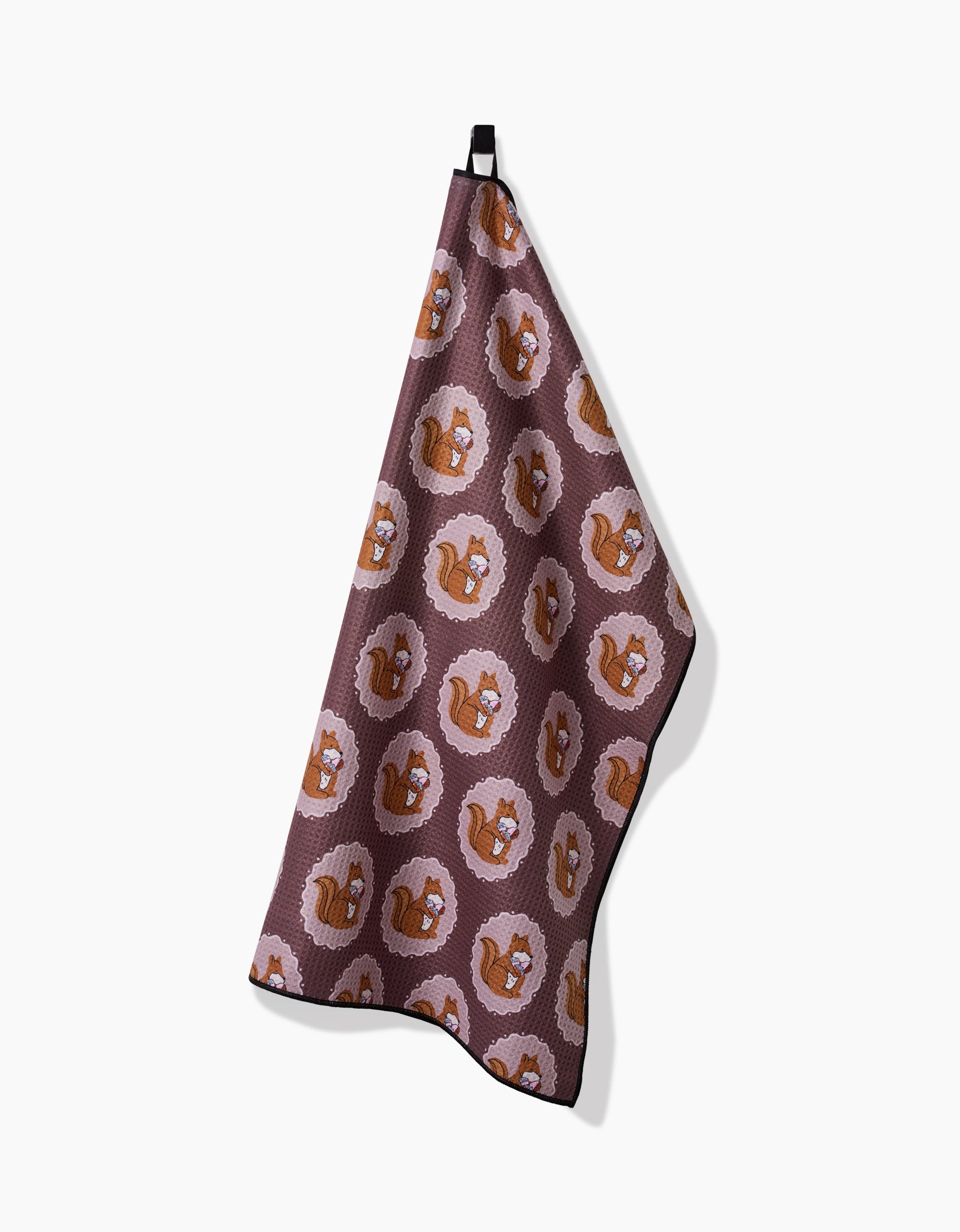 The Megan Roy Squirrels Brown towel features a repeating cartoon squirrel pattern on a brown background, hanging from a black loop against a white backdrop.