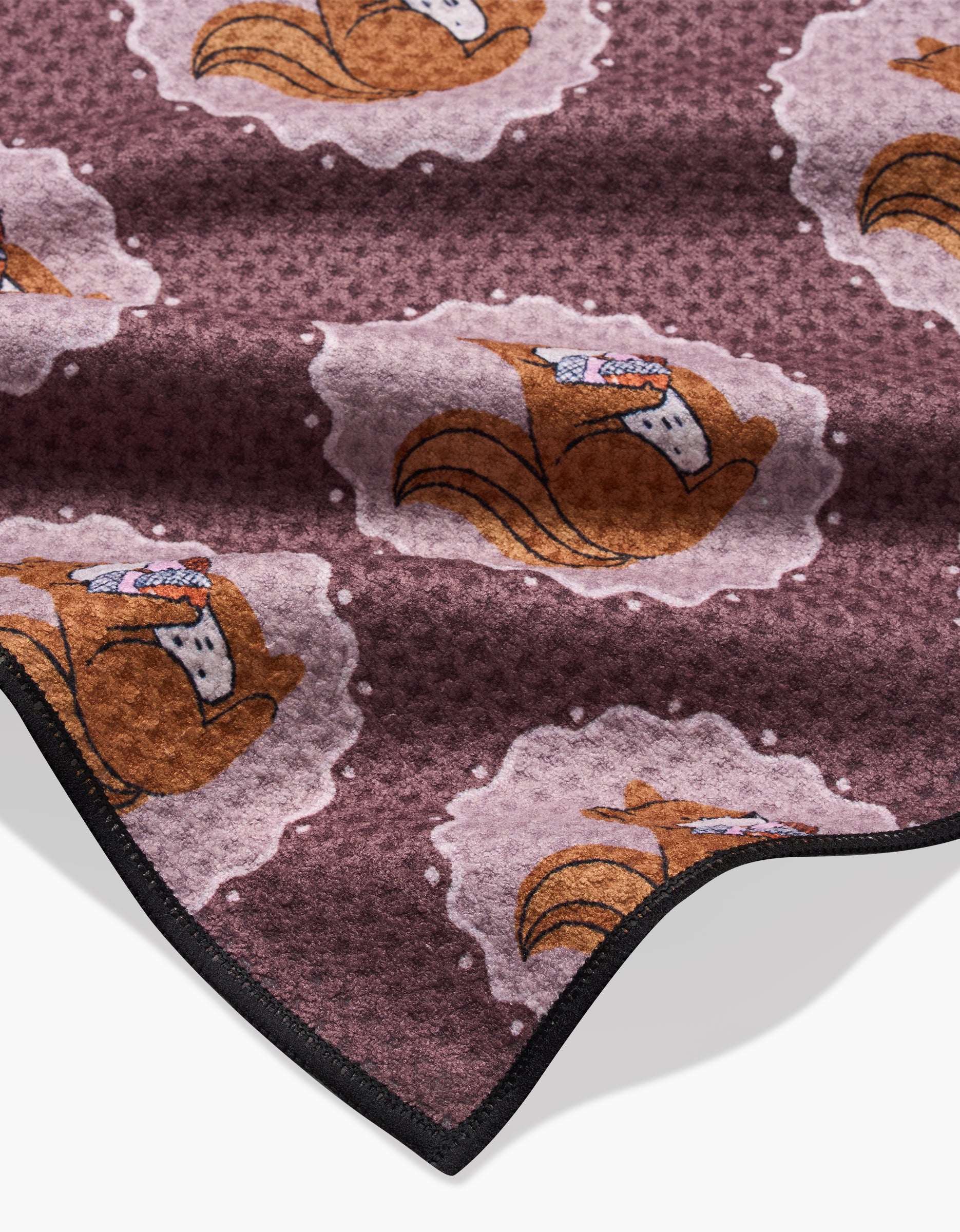 Squirrels Brown by Megan Roy is a soft, eco-friendly brown blanket featuring a repeating pattern of cartoon squirrels wearing scarves among pale, cloud-like shapes, and finished with a black stitched edge.