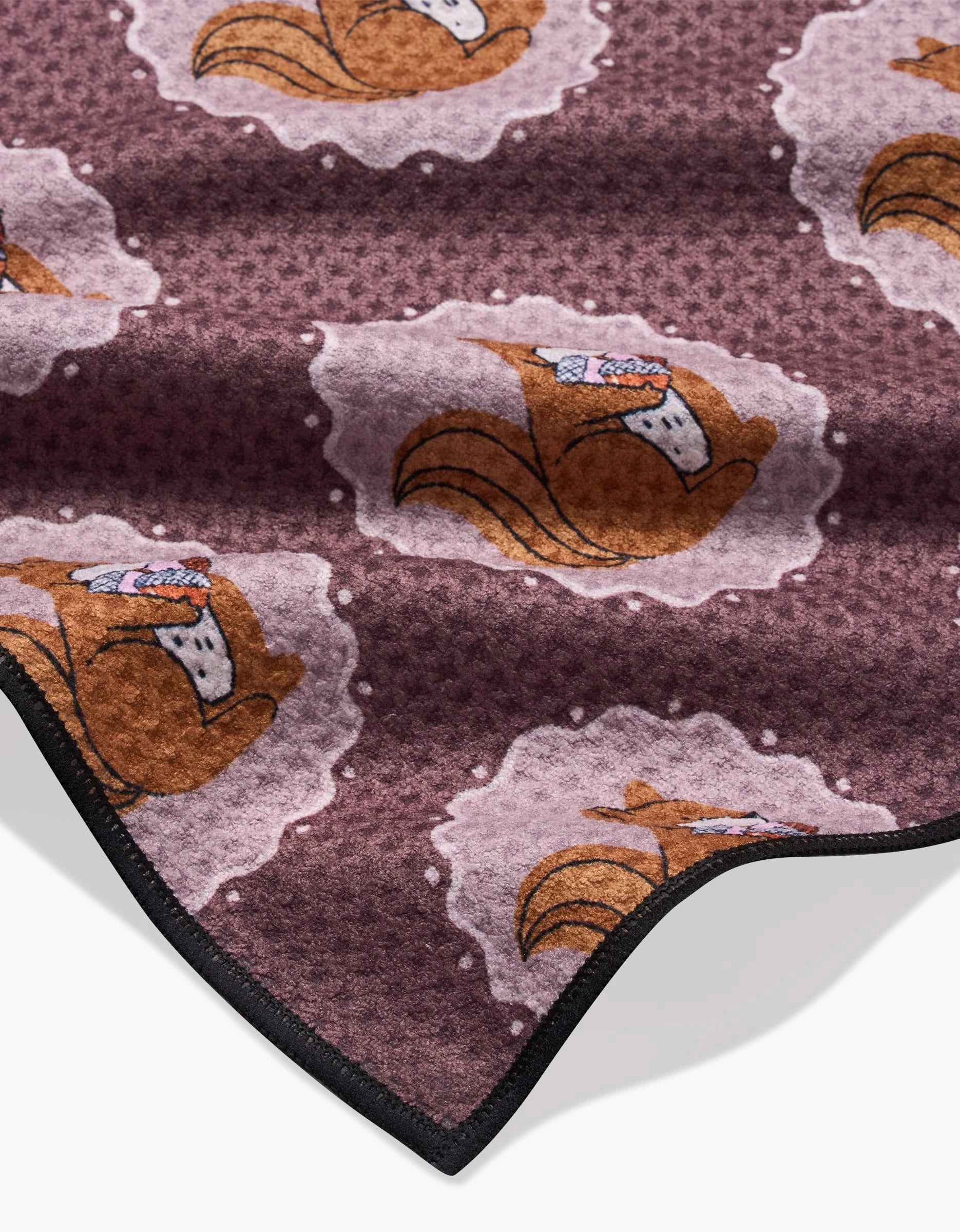Squirrels Brown by Megan Roy is a soft, eco-friendly brown blanket featuring a repeating pattern of cartoon squirrels wearing scarves among pale, cloud-like shapes, and finished with a black stitched edge.
