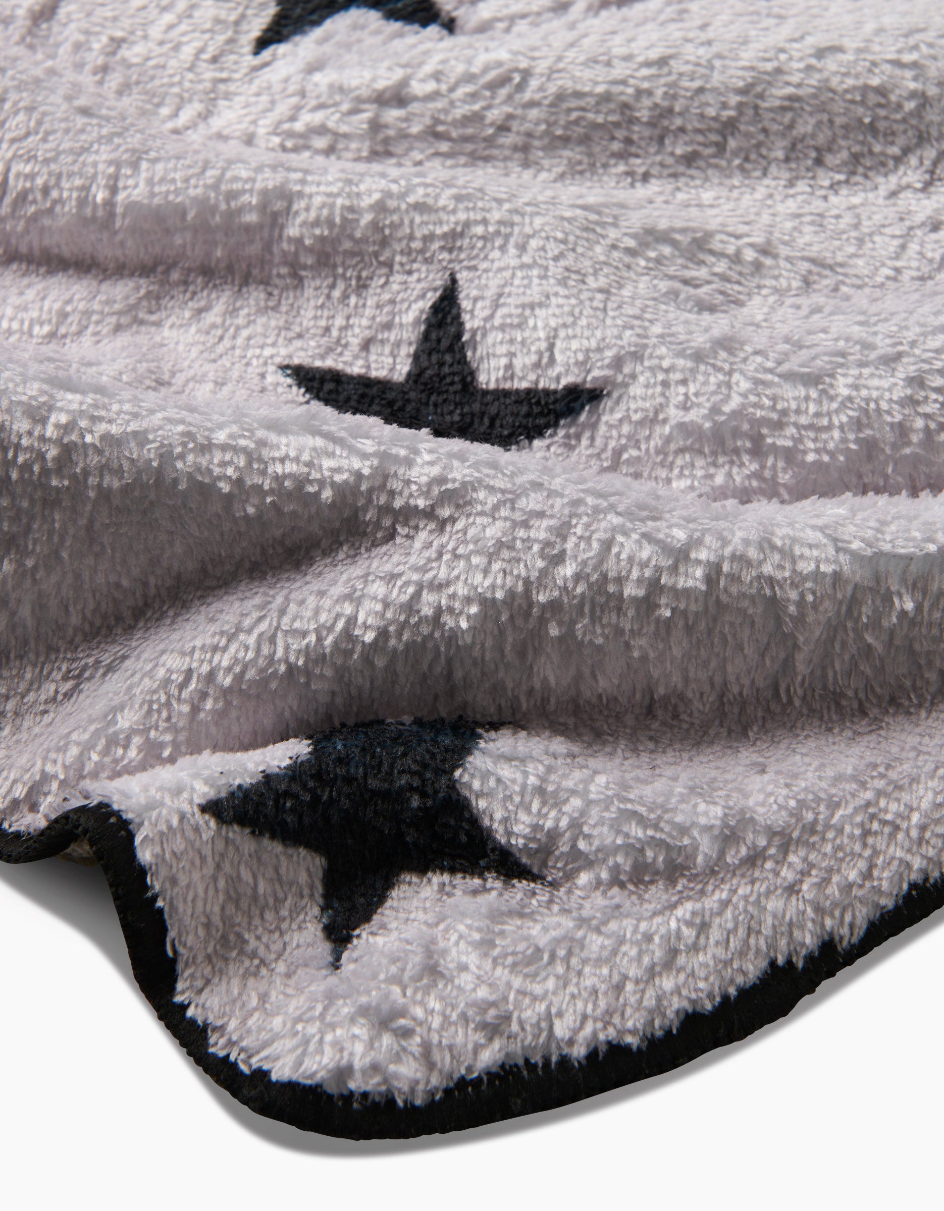 A close-up of Geometry’s Bark blanket, featuring plush, ultra-absorbent recycled fabric in light gray with black star patterns and a black-edged border. The blanket looks cozy and soft.