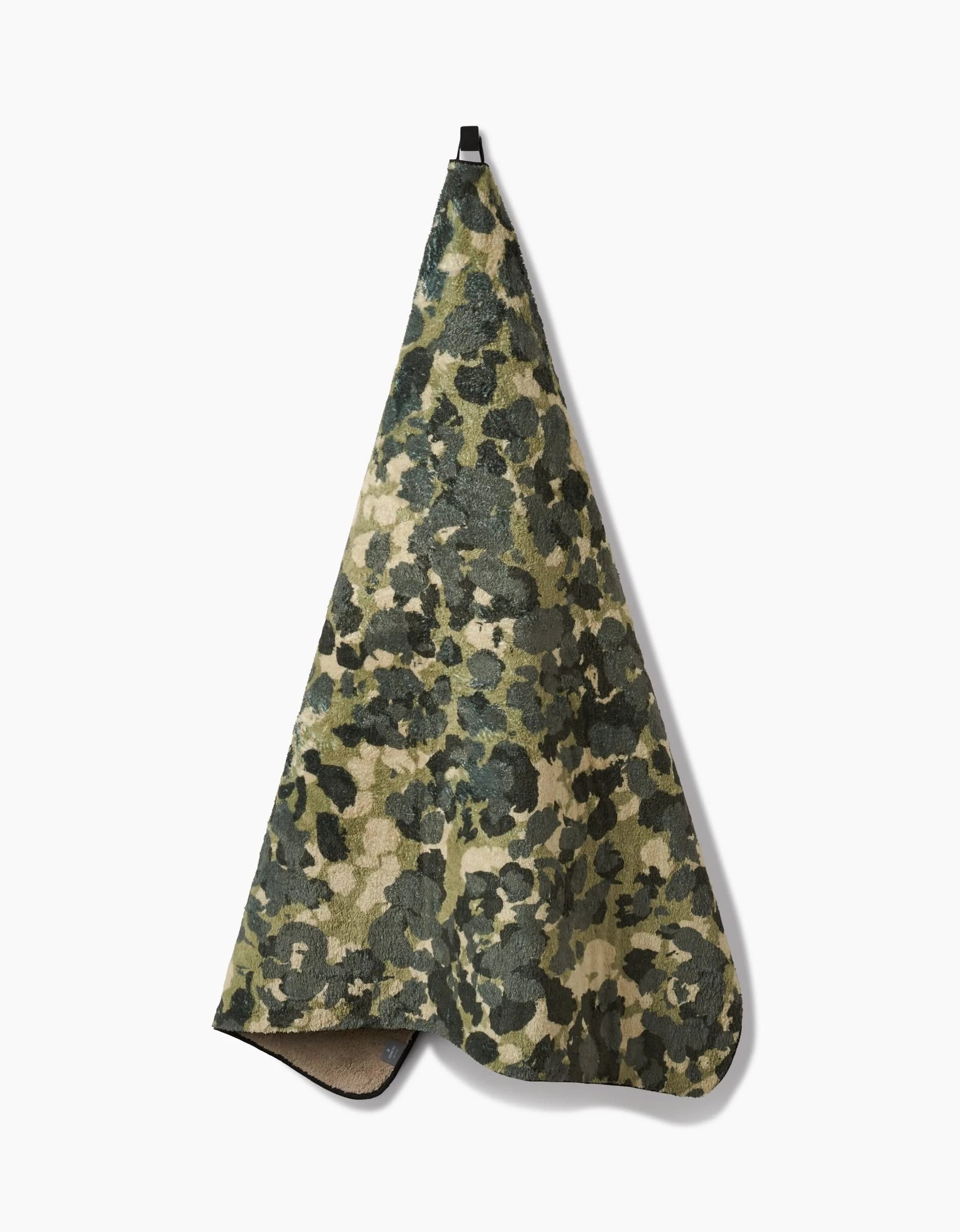 The Geometry Camo towel, featuring an ultra-absorbent design and a green, brown, and beige camouflage pattern, hangs by a black loop against a plain white background.