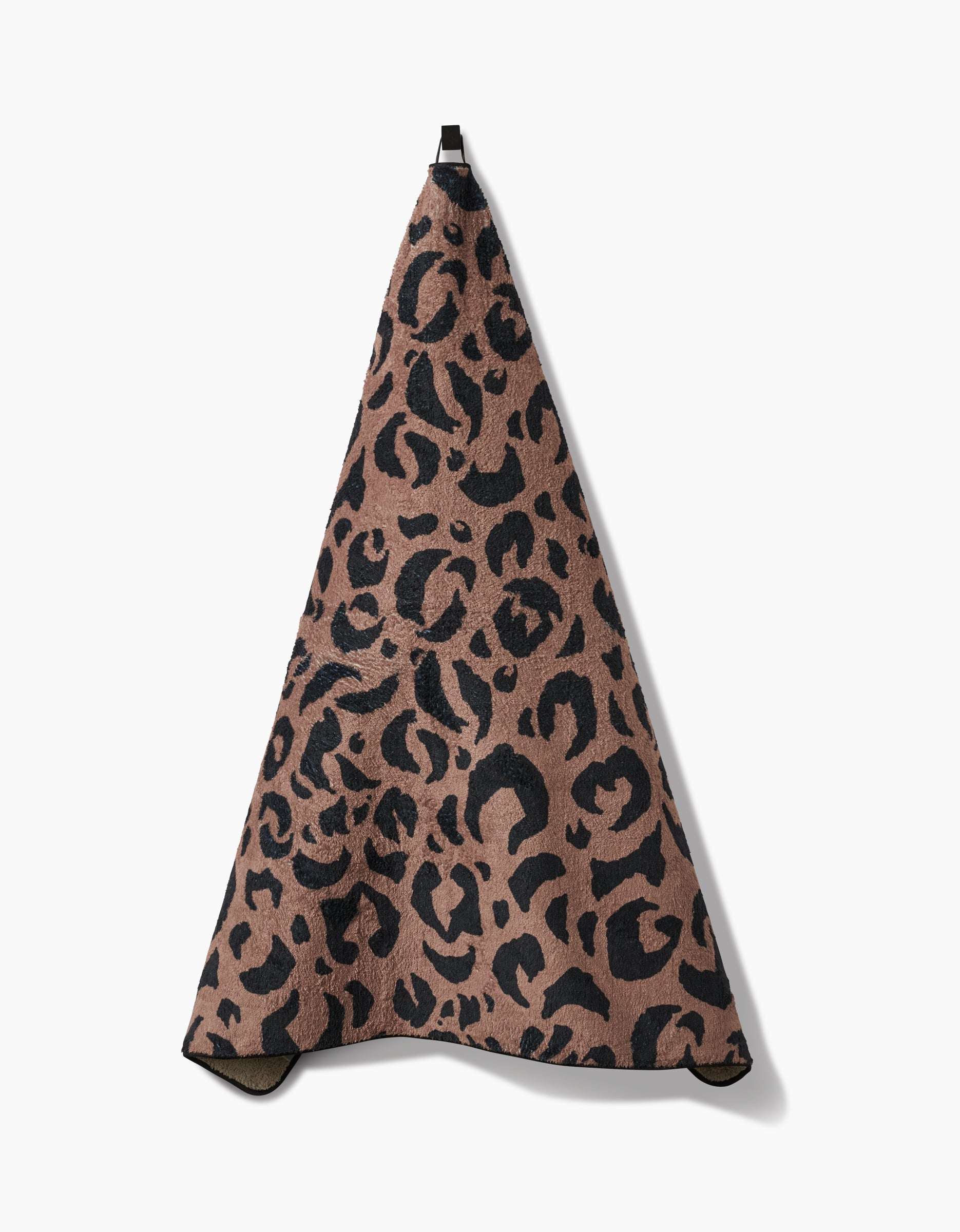 The Geometry Cheetah Hound is a plush dog towel made from recycled materials, featuring a brown base with black leopard print, hanging from a black loop against a white background.