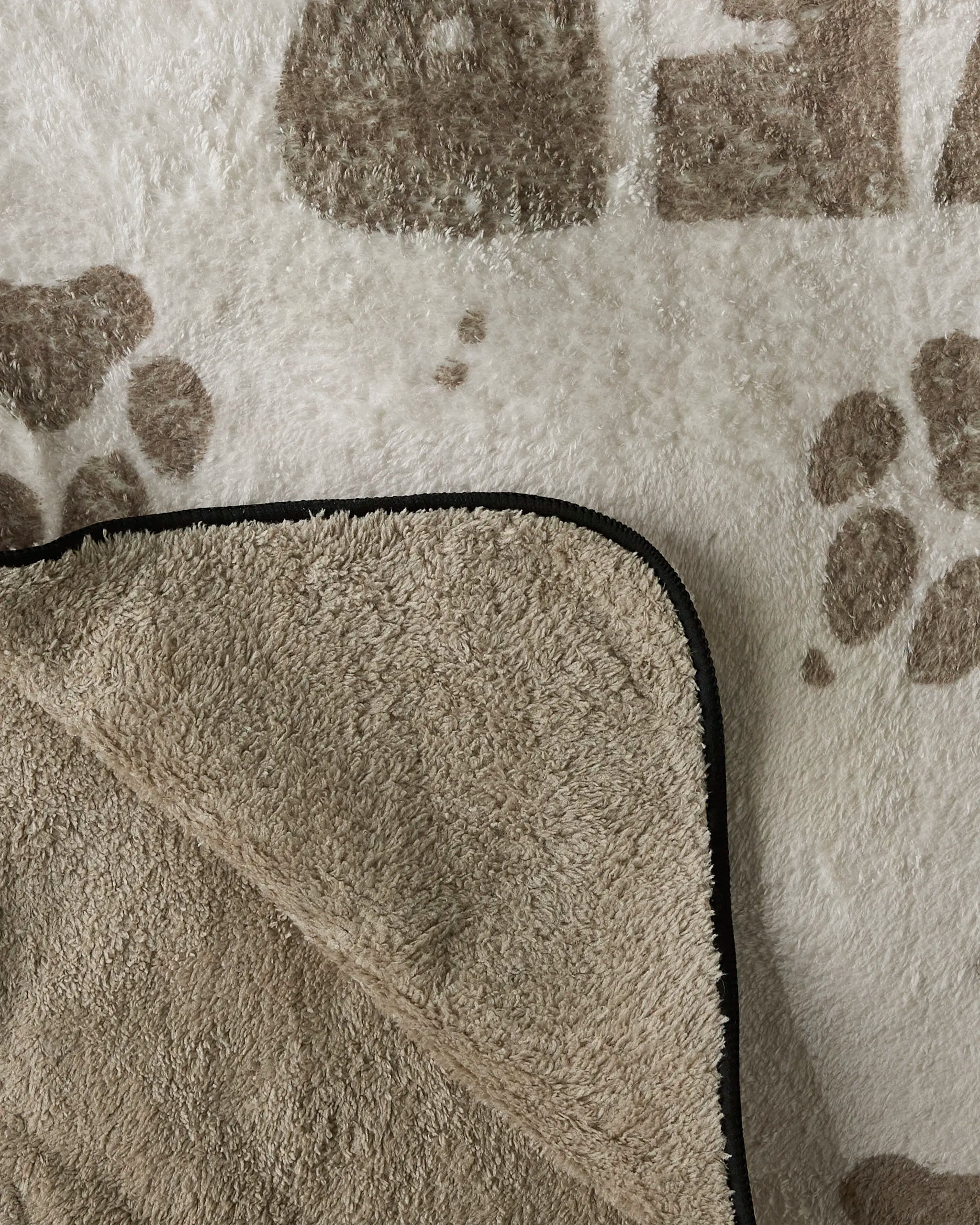 The Fur Ever Friends dog towel by Geometry features beige and white plush fabric with brown paw prints, a black trim, and an ultra-absorbent textured underside. Cozy and practical, it's crafted from recycled materials for eco-friendly comfort.
