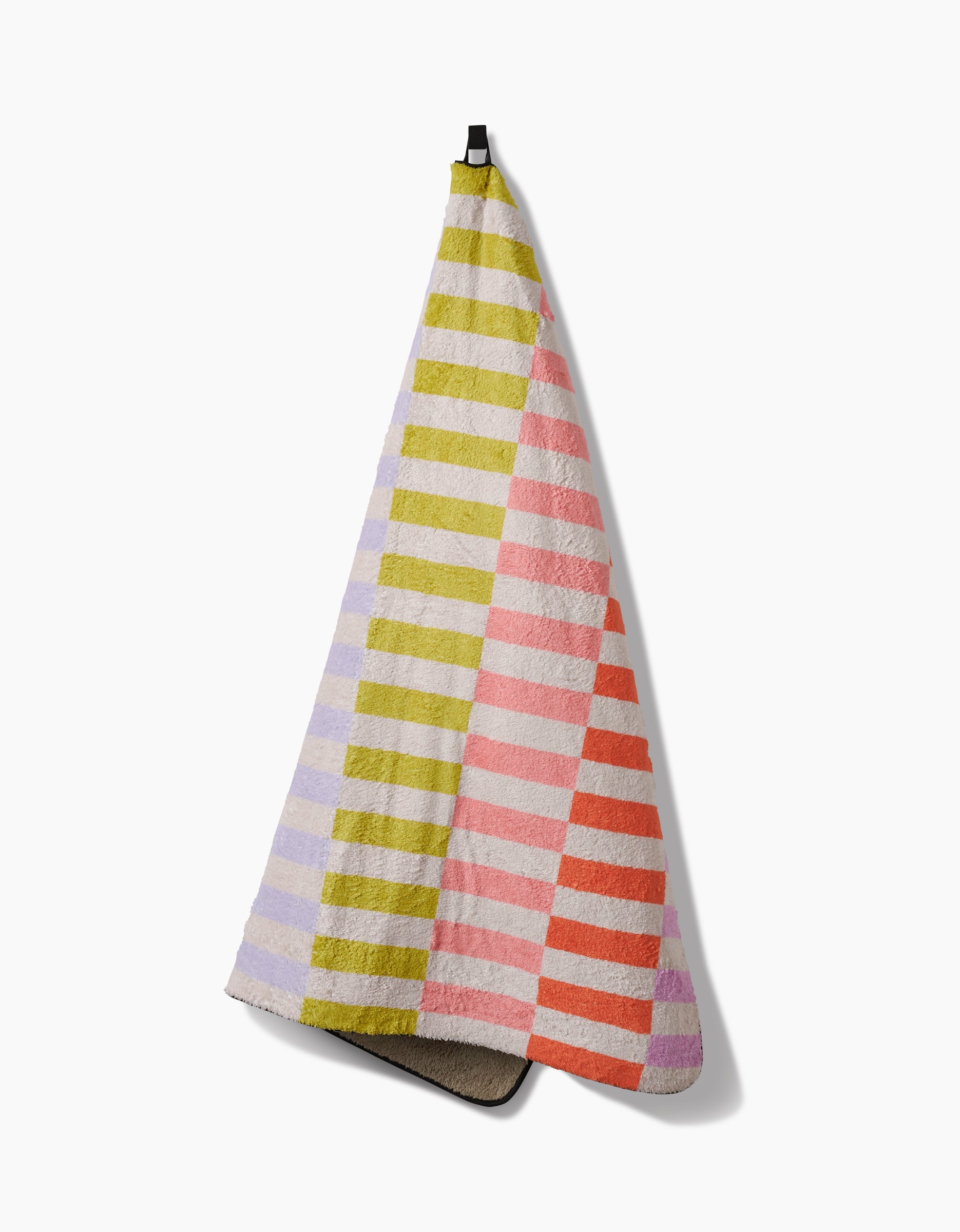 The Geometry Wag Wise plush dog towel, made from recycled materials and showcasing pastel purple, green, pink, and orange stripes, hangs from a hook against a white background.