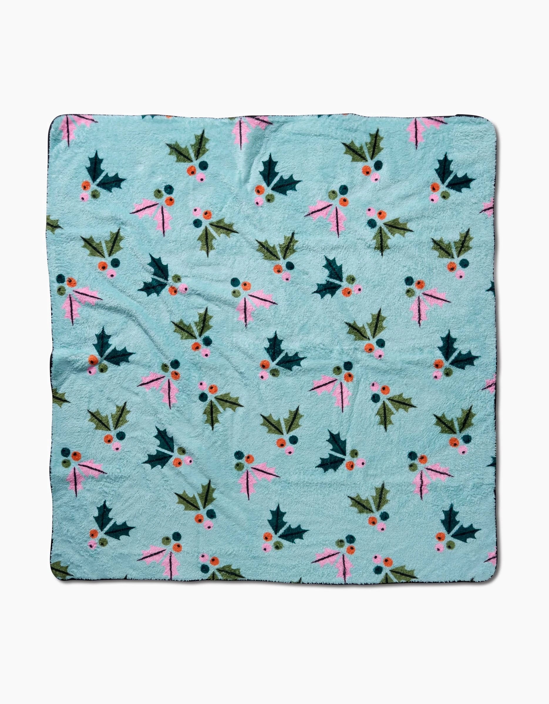 The Berries Mint dog towel by Megan Roy is a light blue, ultra-absorbent towel with holly leaves, red berries, and pink ribbons in a repeating pattern, shown flat on a white background.