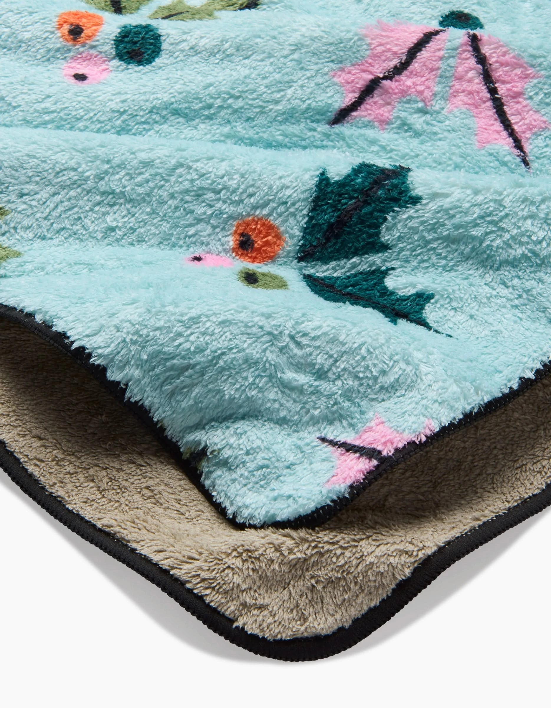 A close-up of the Megan Roy Berries Mint dog towel, featuring a light blue top with a colorful holiday floral pattern, a contrasting tan underside, and a black border.