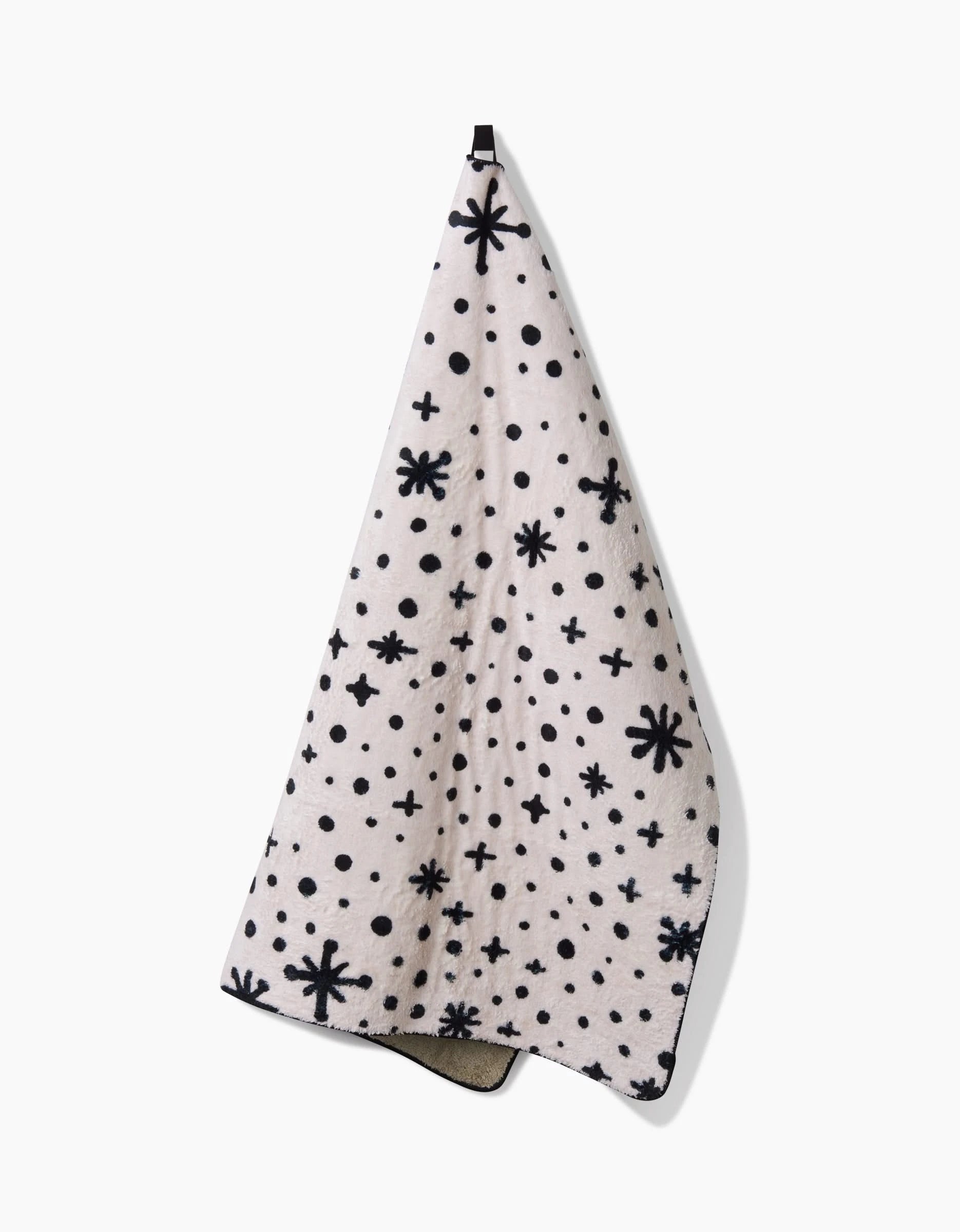 The Amy MacCready Estrella White dog towel, featuring black starburst, dot, and plus sign patterns, hangs from a hook against a white background.