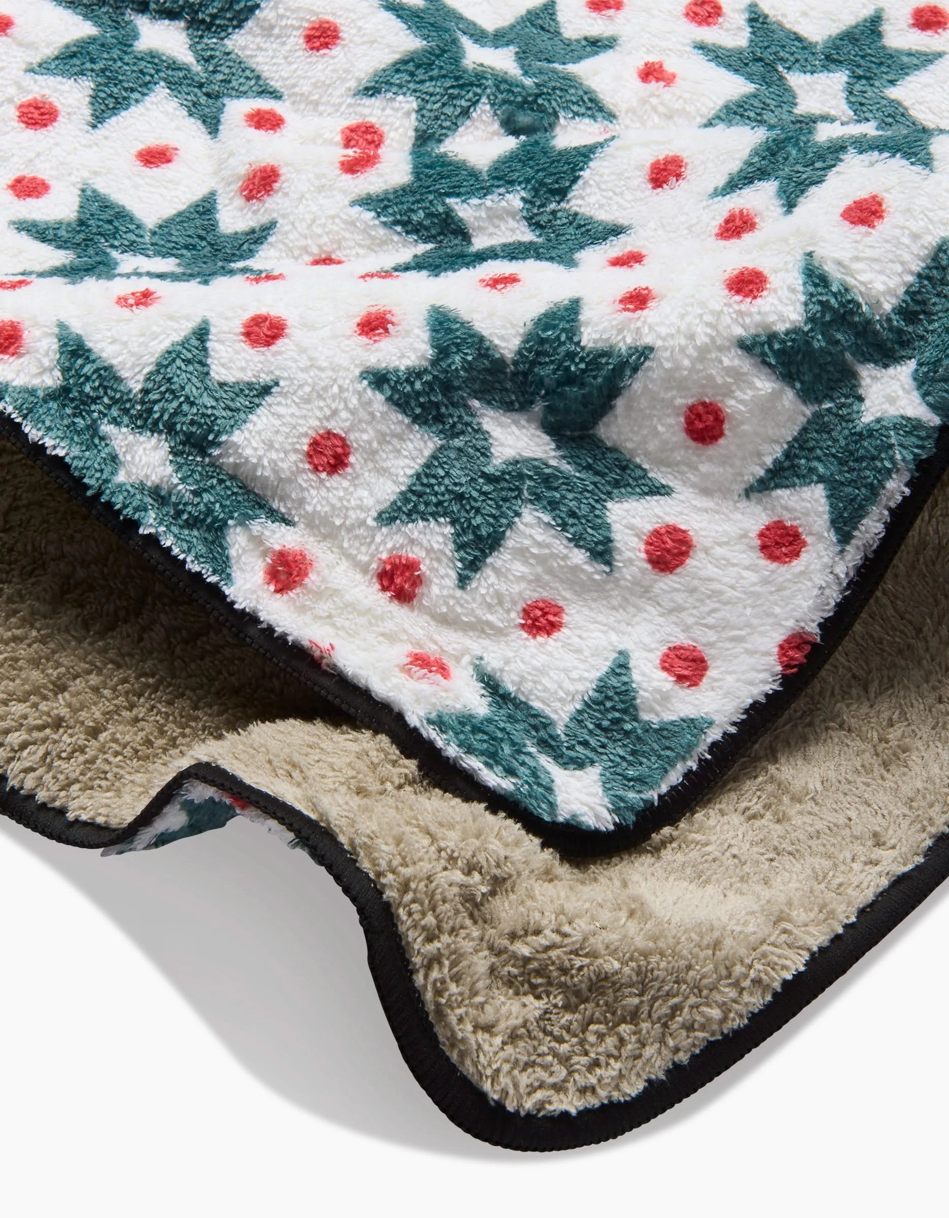 A close-up of the Geo Star dog towel by Charlie Rowan Designs, featuring soft fleece with green stars and red dots on white. Folded to show a beige plush underside and black trim—ideal for keeping your pup cozy and dry.