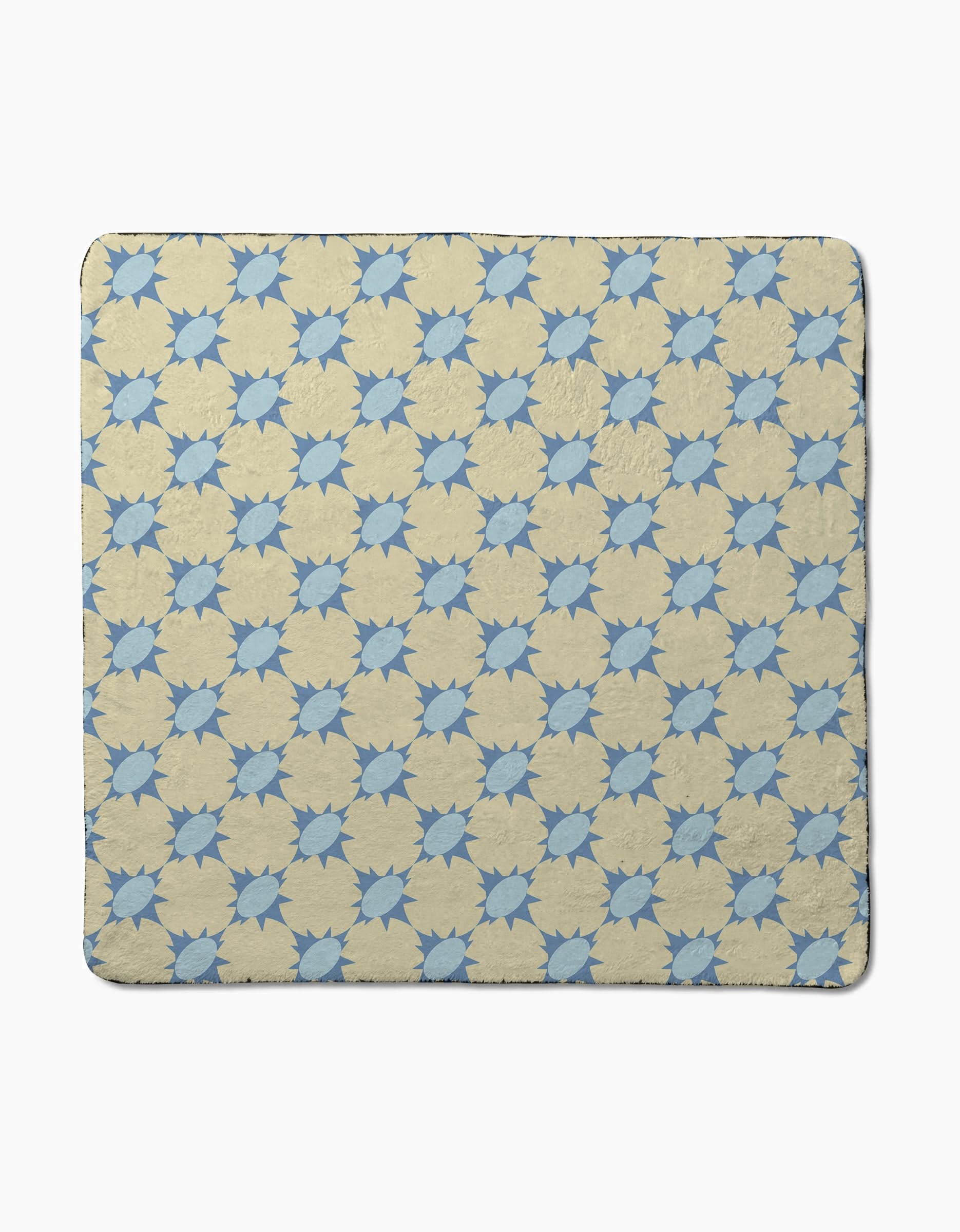 The Spiky quilt by Geometry features a repeating blue eight-pointed star pattern on beige, crafted from recycled materials. Shown laid flat on a plain white background.