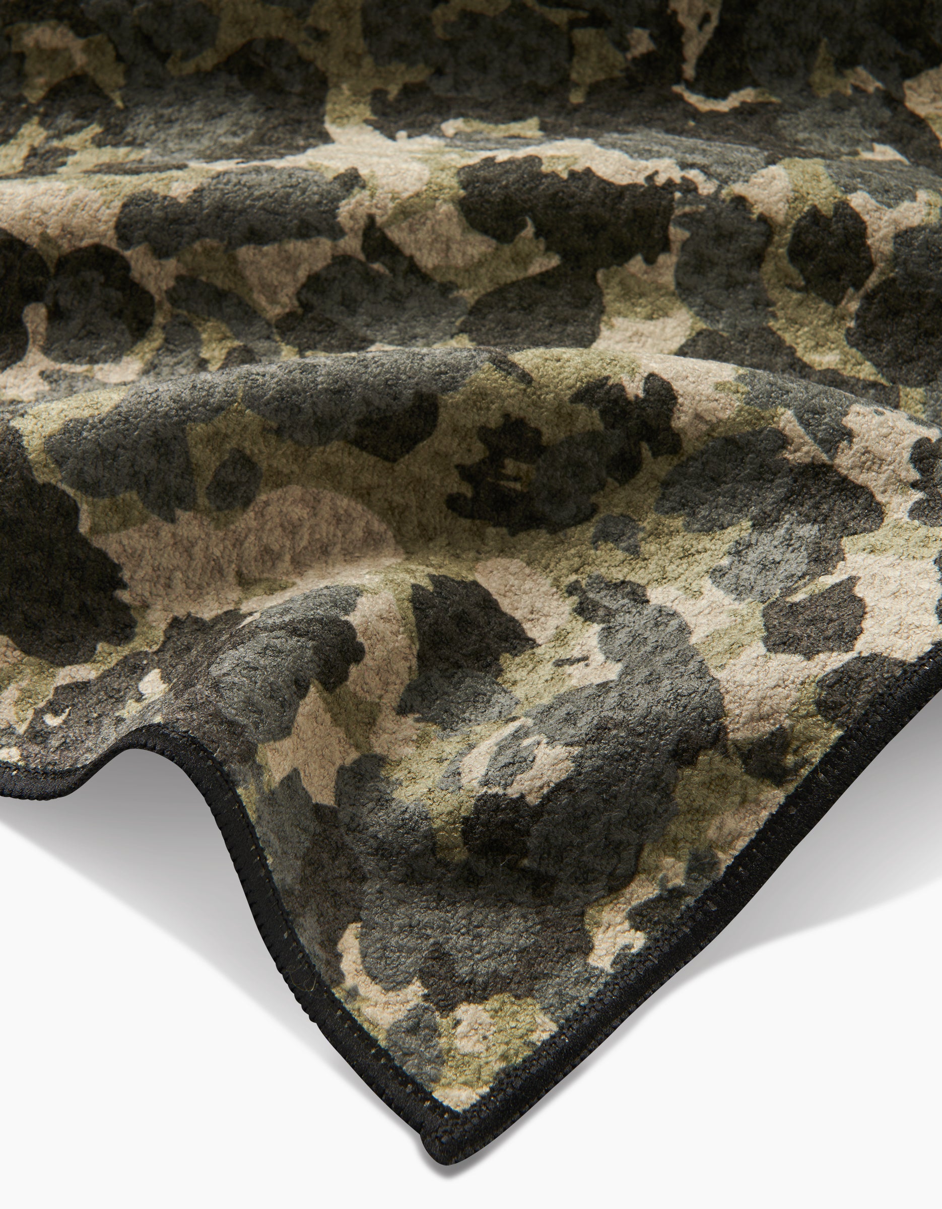 A close-up of the Geometry Camo blanket, made from ultra-absorbent Geoweave fleece in a green, brown, and black camouflage pattern with curved black stitching, shown against a white background for maximum comfort.
