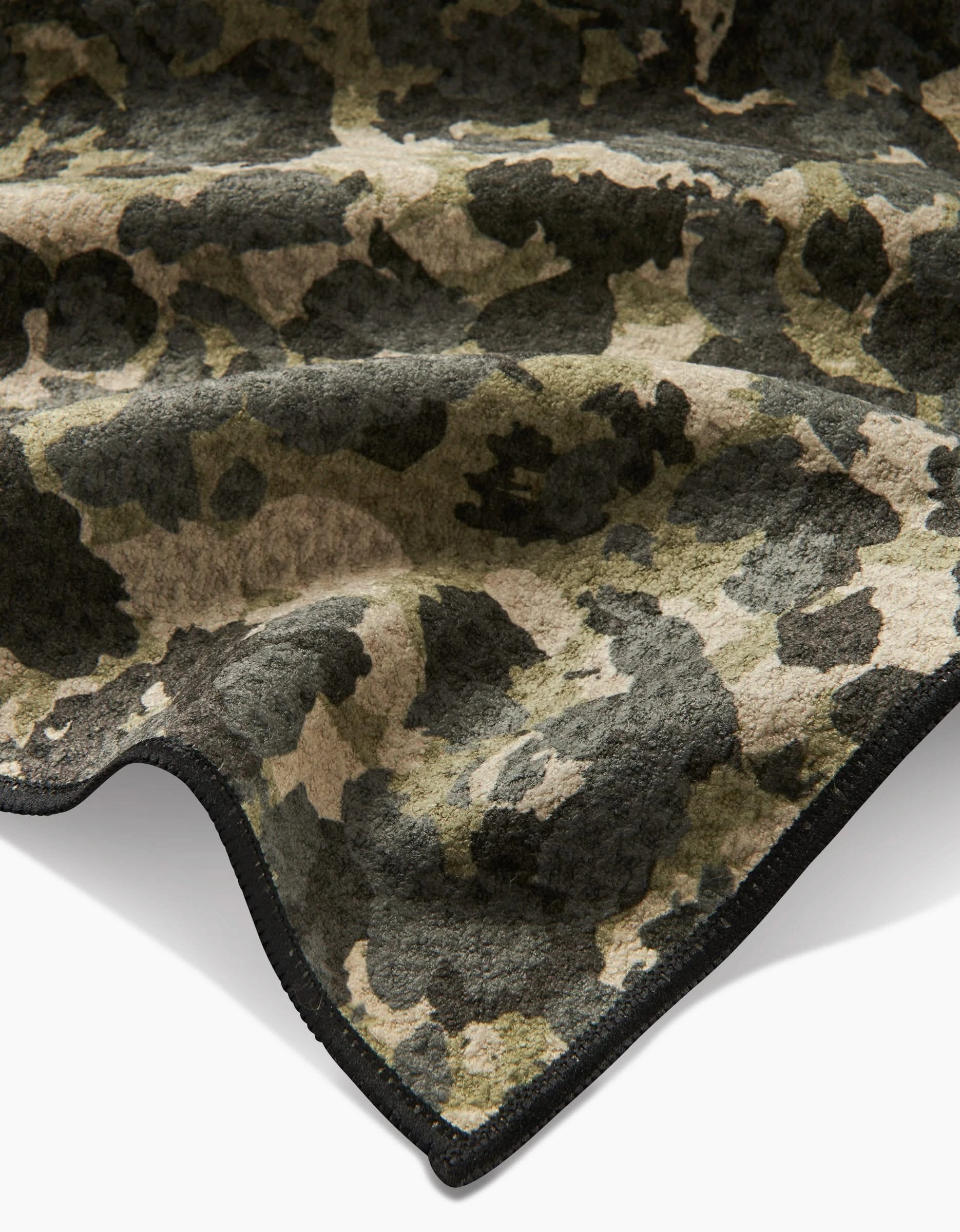 A close-up of the Geometry Camo blanket, made from ultra-absorbent Geoweave fleece in a green, brown, and black camouflage pattern with curved black stitching, shown against a white background for maximum comfort.