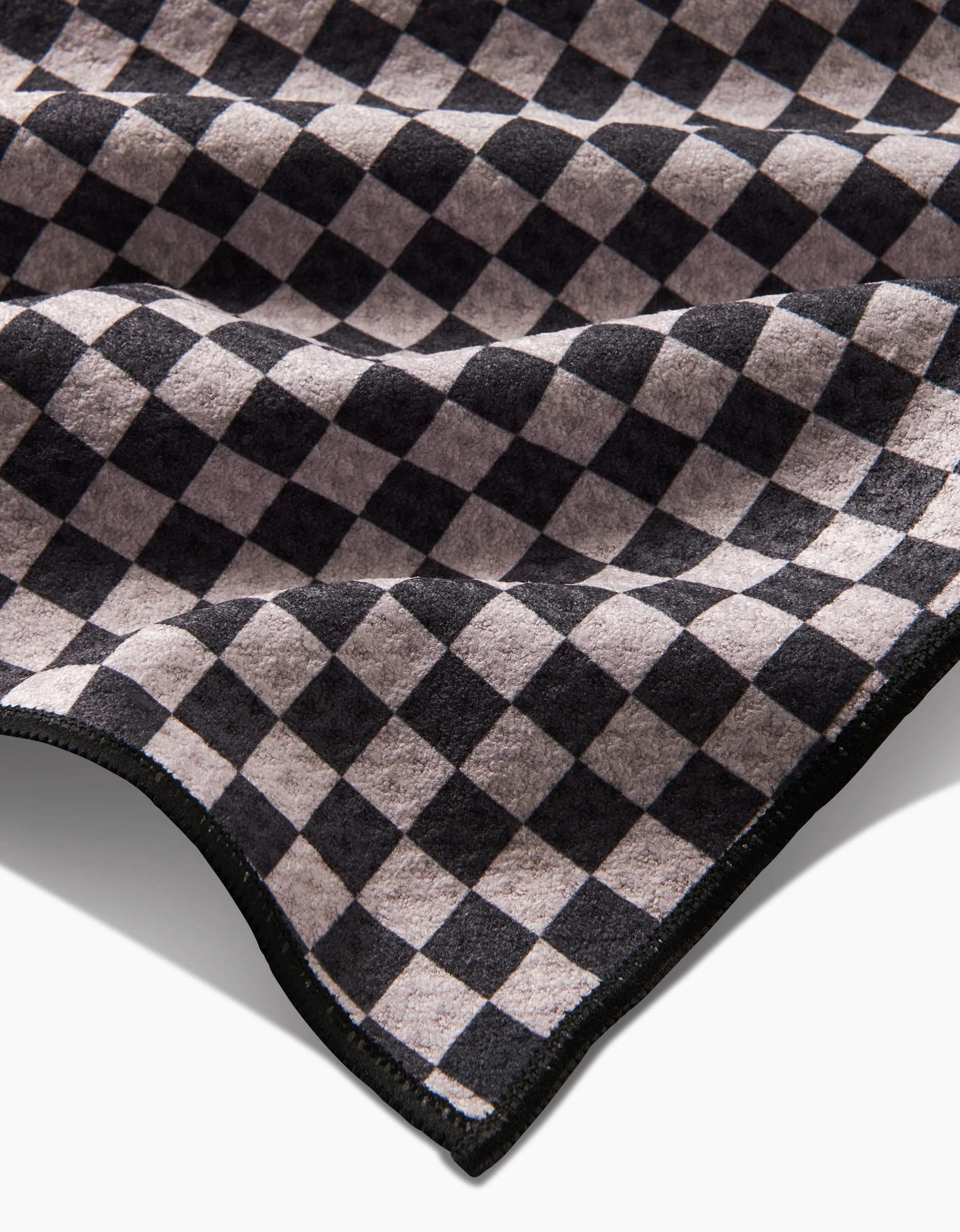 A close-up of Cool Pup by Geometry, featuring soft Geoweave fabric with a black and beige checkerboard pattern. Slightly folded at the edges, this ultra-absorbent towel is perfect for drying your pets paws.