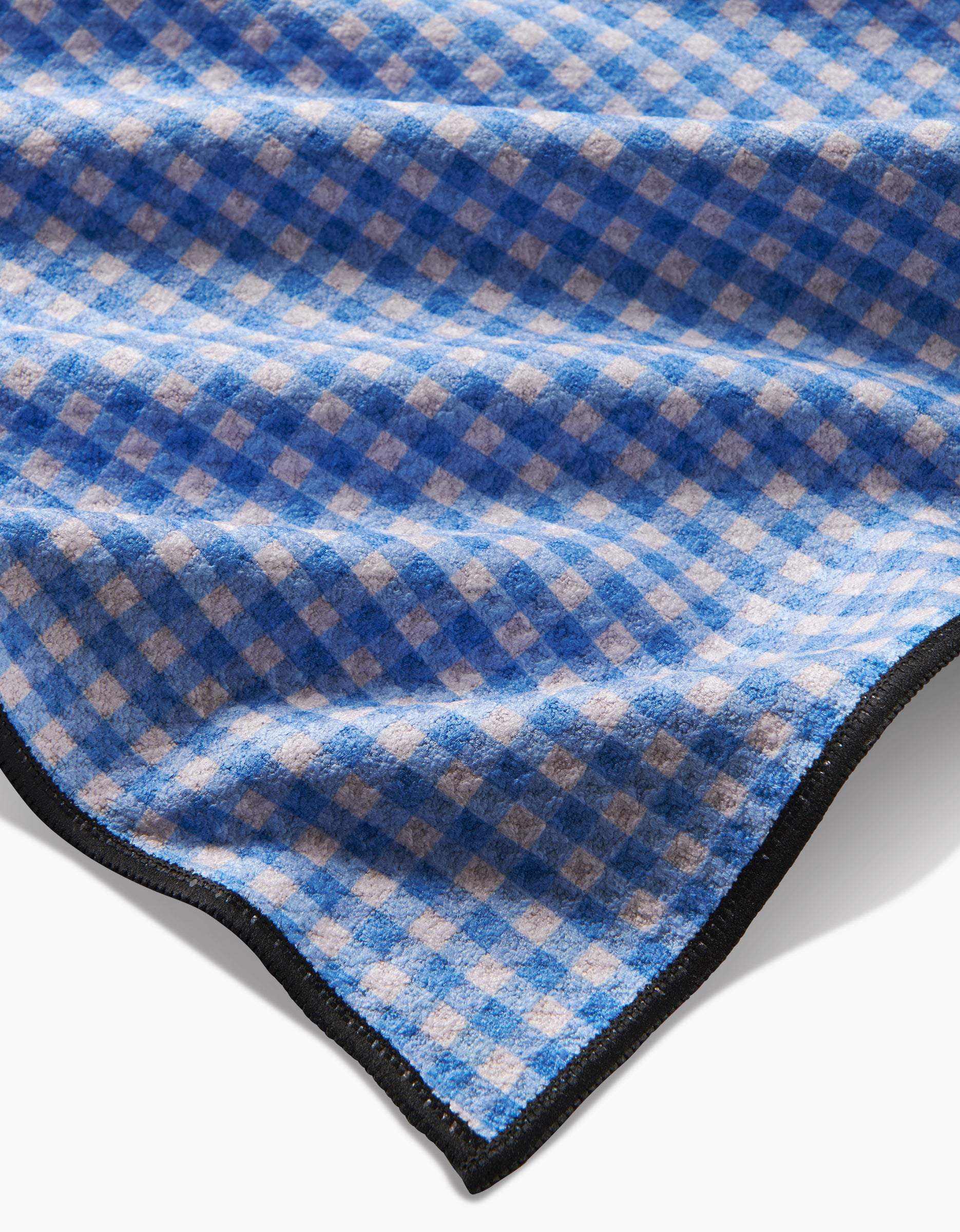 A close-up of the Geometry Dog Delight towel, crafted from Geoweave fabric, displays a blue and white checkered pattern, ultra-absorbent softness, and neatly black-trimmed edges.