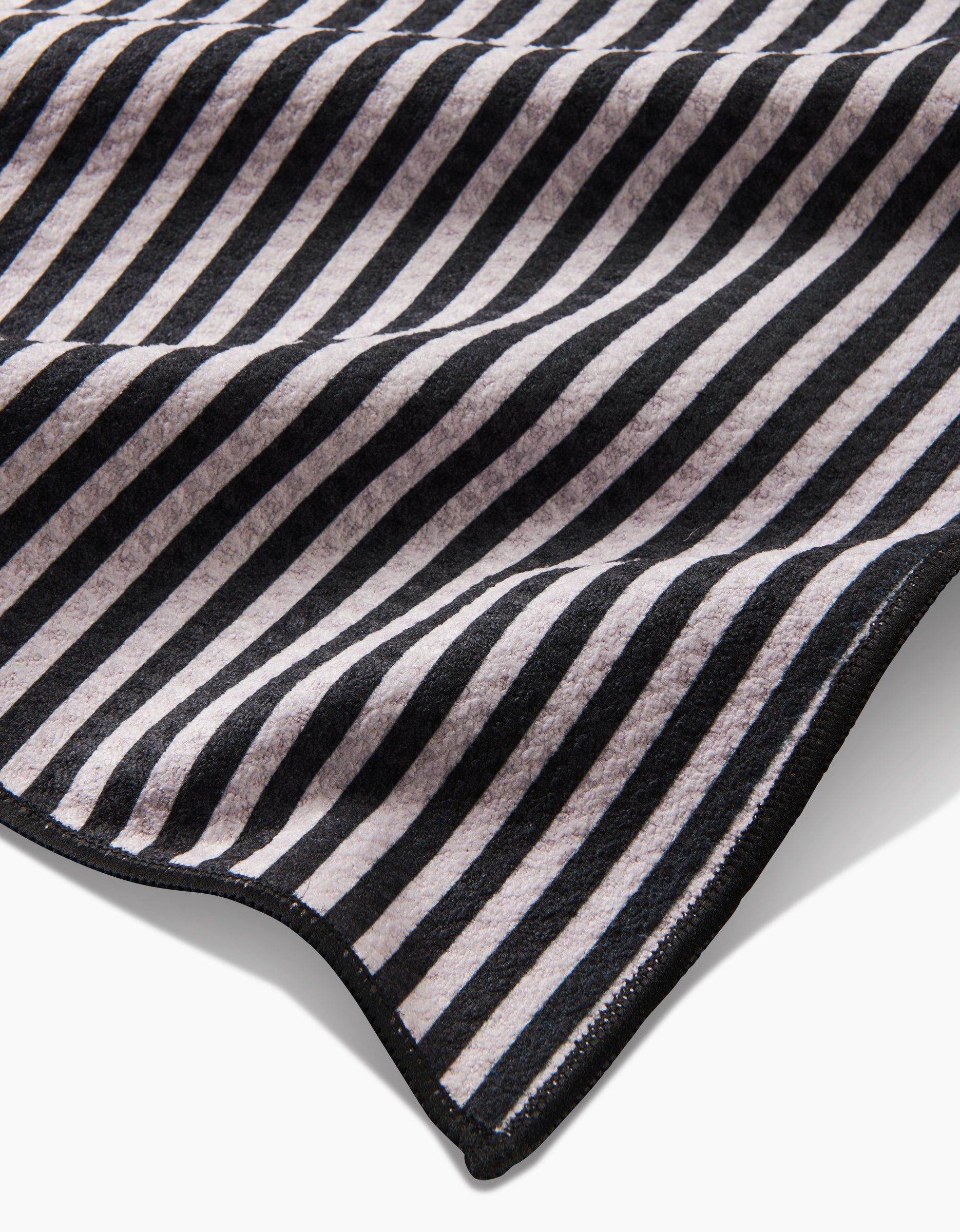 A close-up of the Good Pup Paw Towel by Geometry, made from recycled materials with black and white diagonal stripes, a wavy texture, and a stitched black edge.