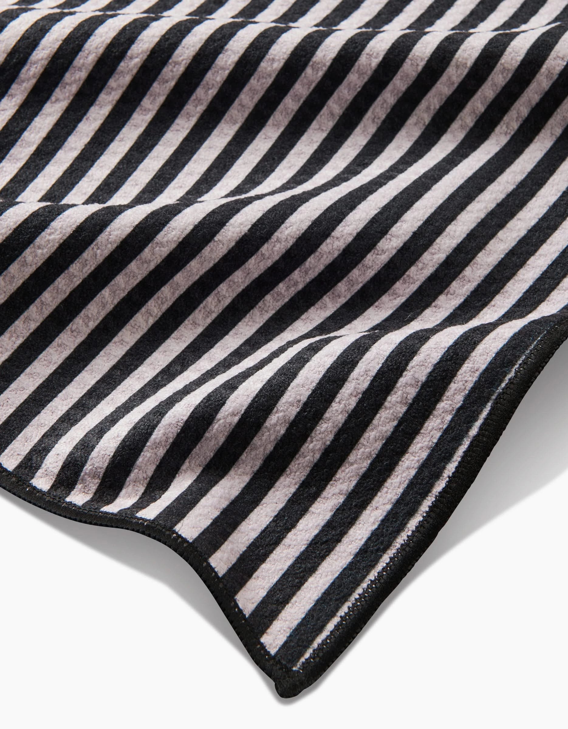 A close-up of the Good Pup Paw Towel by Geometry, made from recycled materials with black and white diagonal stripes, a wavy texture, and a stitched black edge.