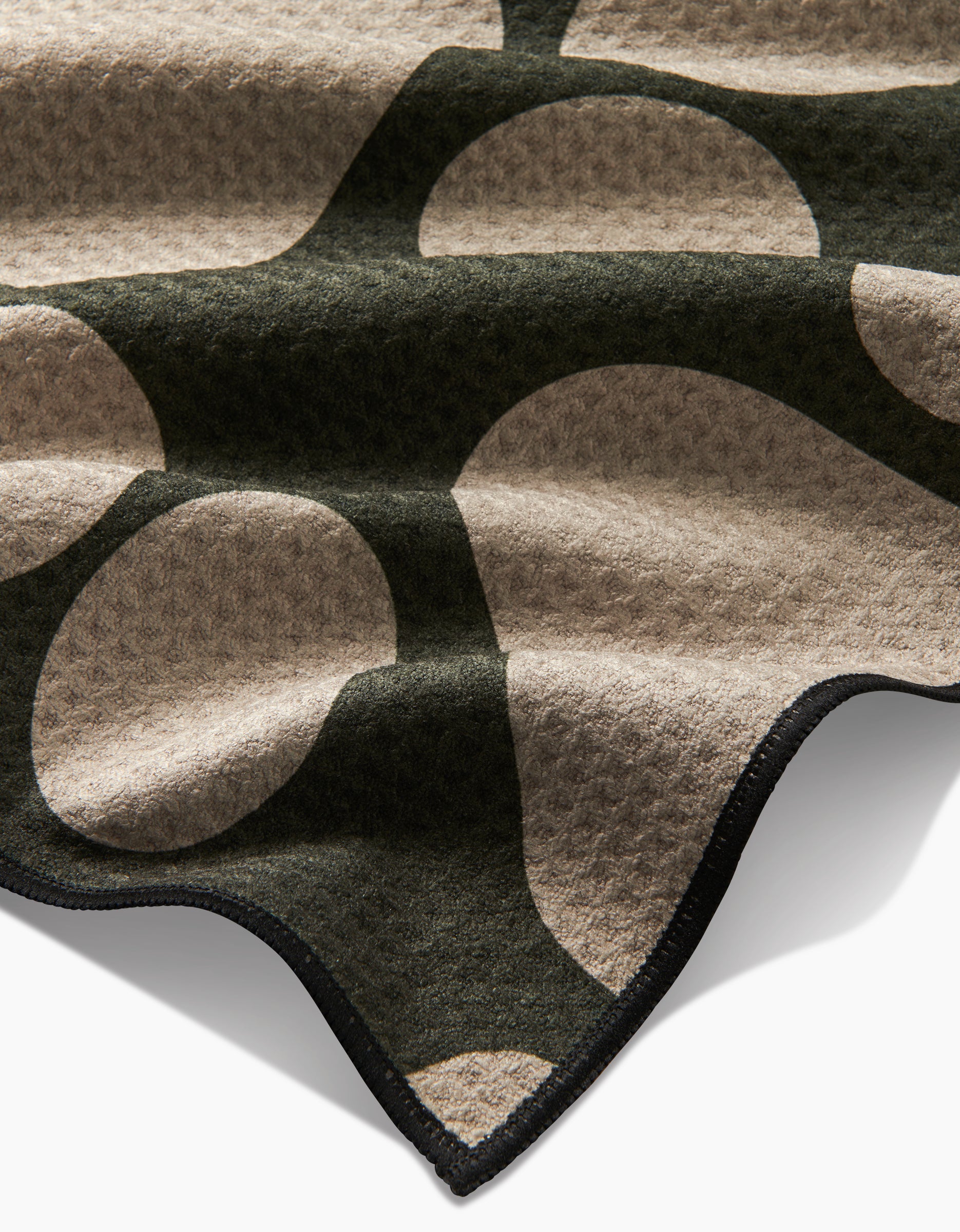 A close-up of Geometrys Paw Prints towel, crafted from recycled materials with a bold beige and dark green abstract pattern and soft texture, featuring wavy edges trimmed in black.
