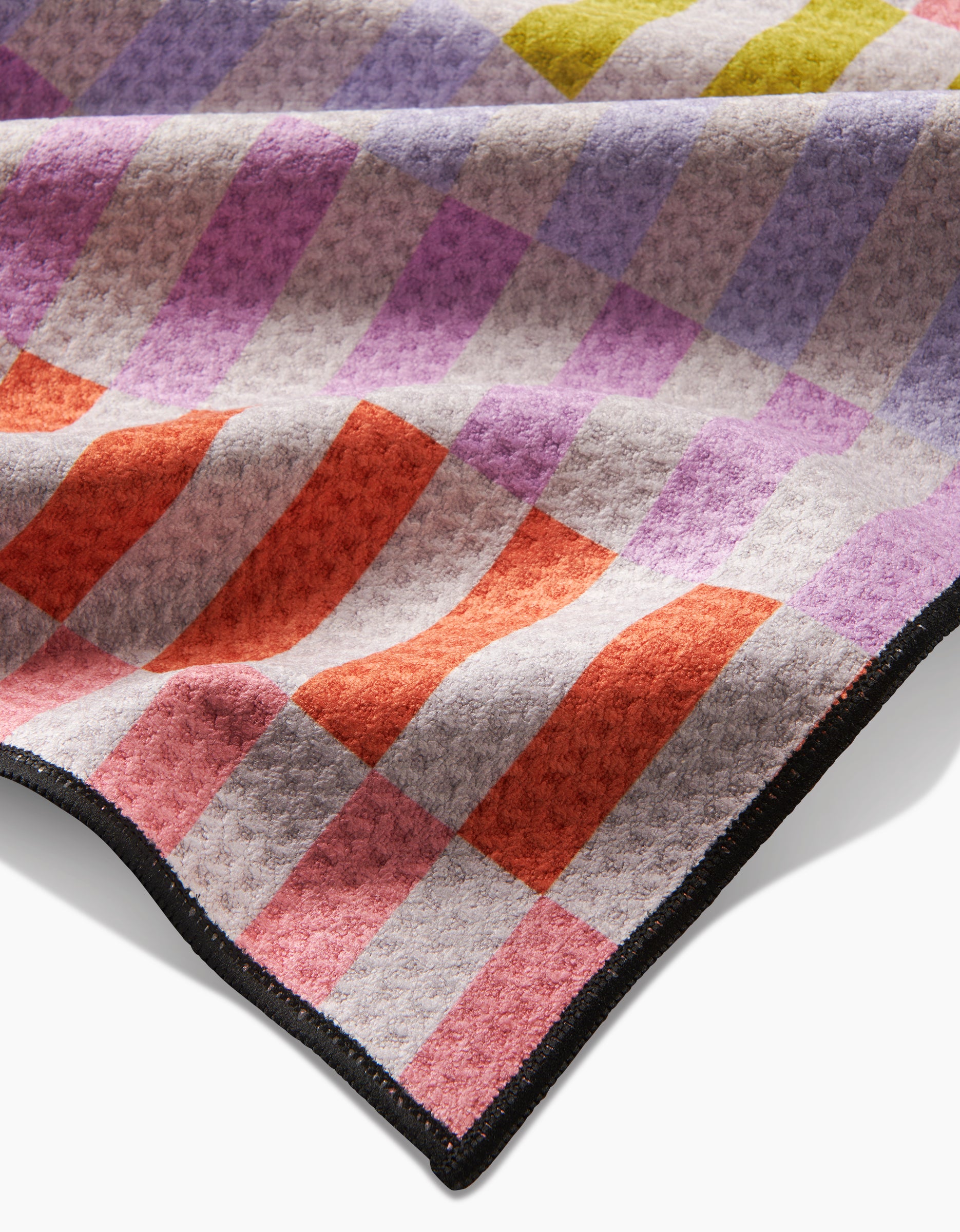 A close-up of Geometrys Wag Wise blanket shows its soft, textured Geoweave fabric with a checkered purple, pink, red, orange, and yellow pattern. This ultra-absorbent blanket features a black stitched edge and is softly folded.