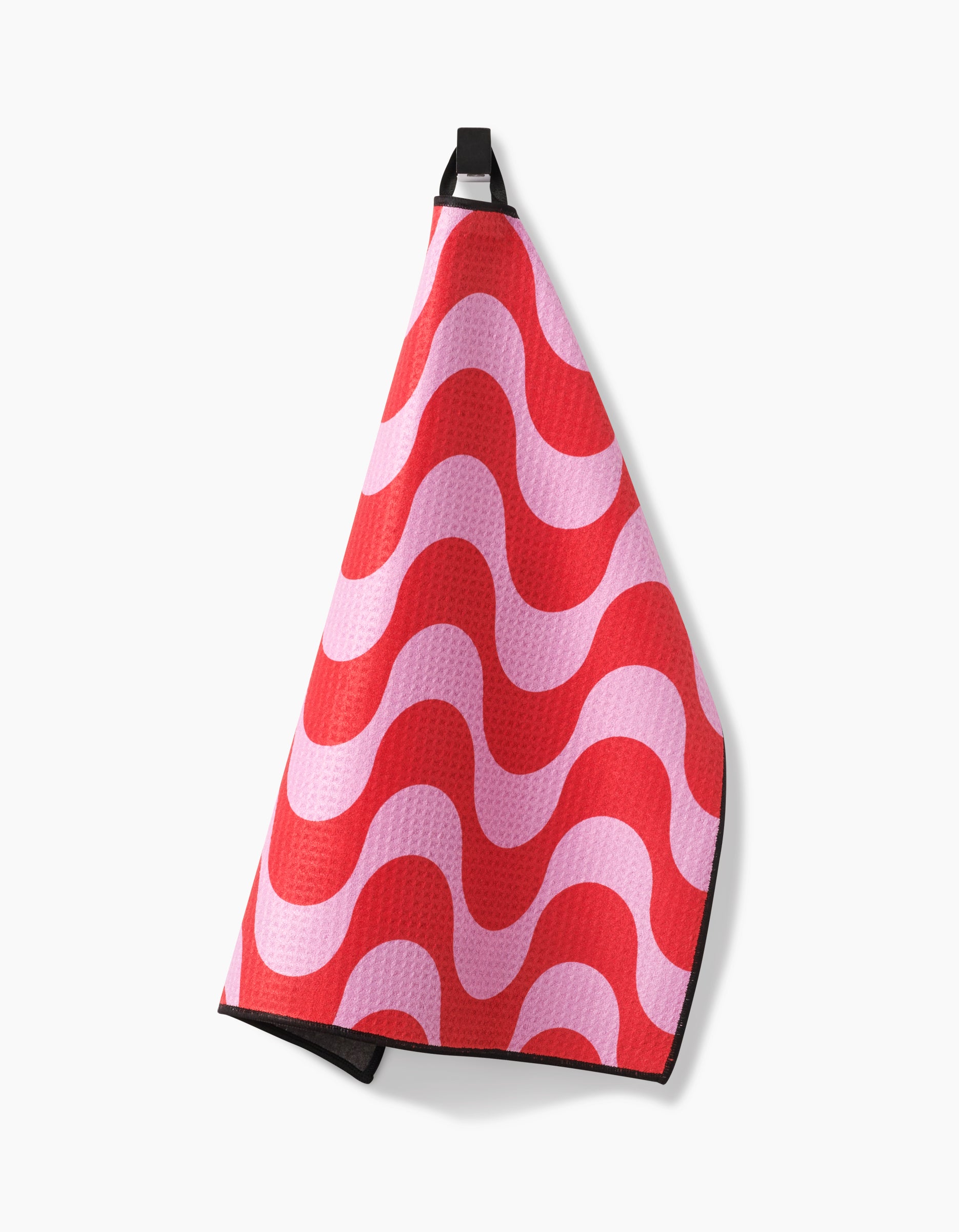 The Geometry Waves towel, featuring a pink and red wavy pattern, hangs from a black loop against a plain white background.