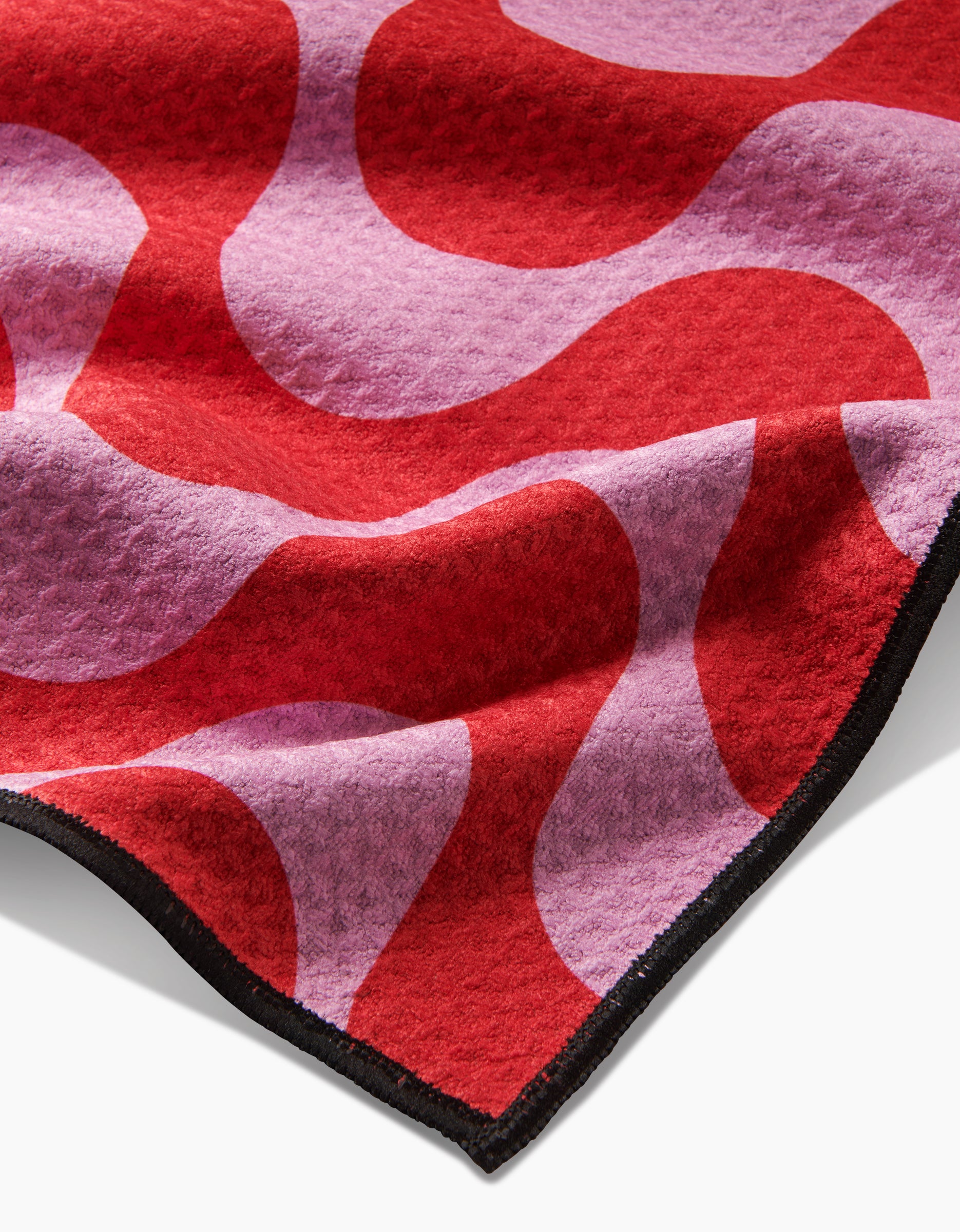 A close-up of the Geometry Waves towel, crafted from ultra-absorbent Geoweave fabric, with a wavy red and pink design and a black stitched border.