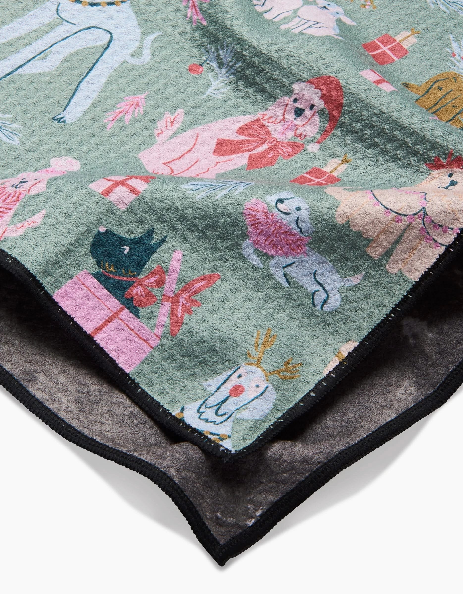 A close-up of the Christmas Doggos recycled PET towel by Janna Sue Design, featuring green textured fabric with festive dogs in hats and scarves, gift boxes, holiday decorations, and a black edge.