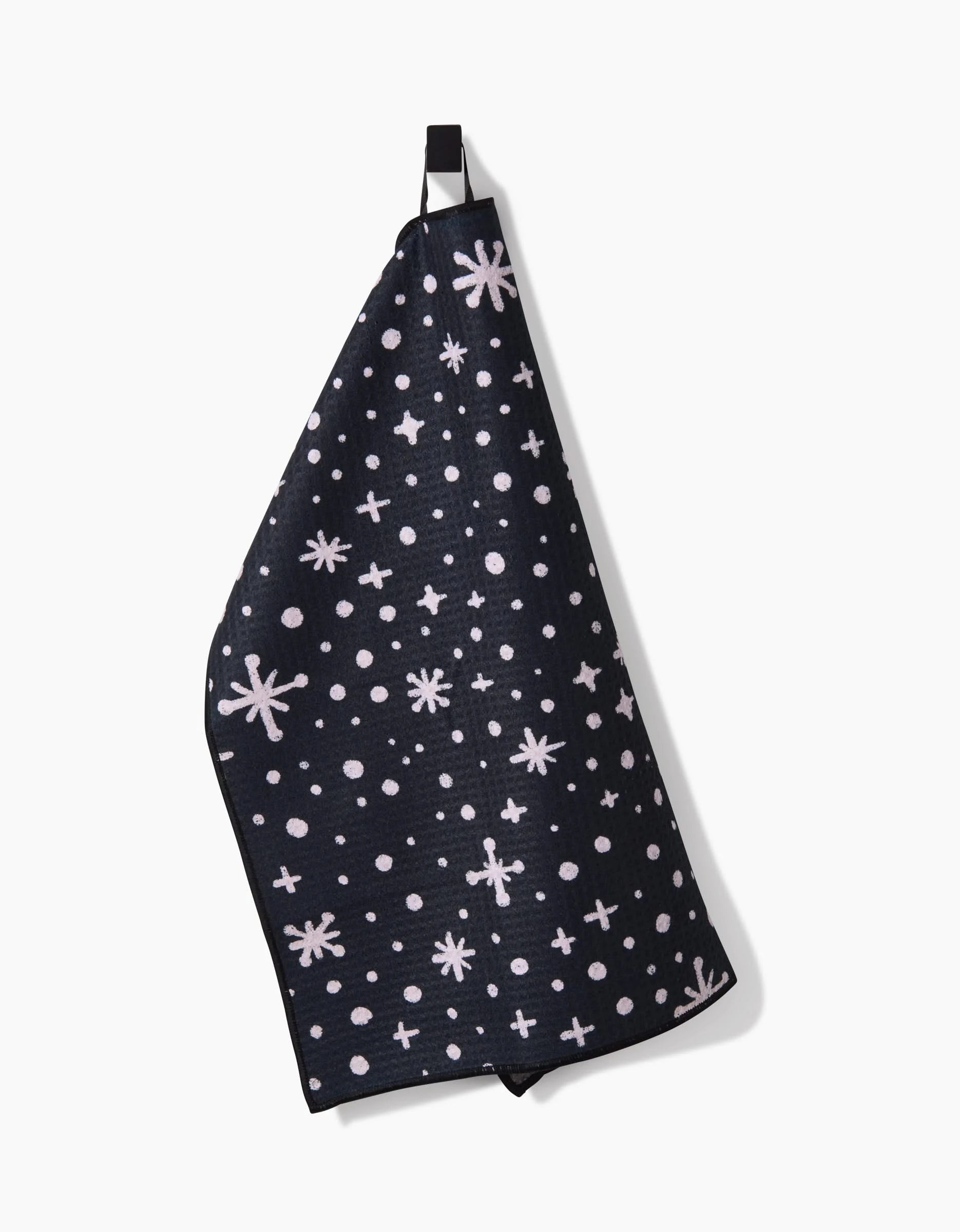 The Estrella towel by Amy MacCready is made from black recycled PET, features a hanging loop, and is decorated with white stars, dots, and plus signs.