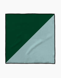 The Minted Oasis Paw Towel by Geometry features a rectangular shape with a diagonal split—dark green on the top left and light gray on the bottom right. Crafted from Geoweave™ fabric, it has a soft, subtly textured surface with visible creases.