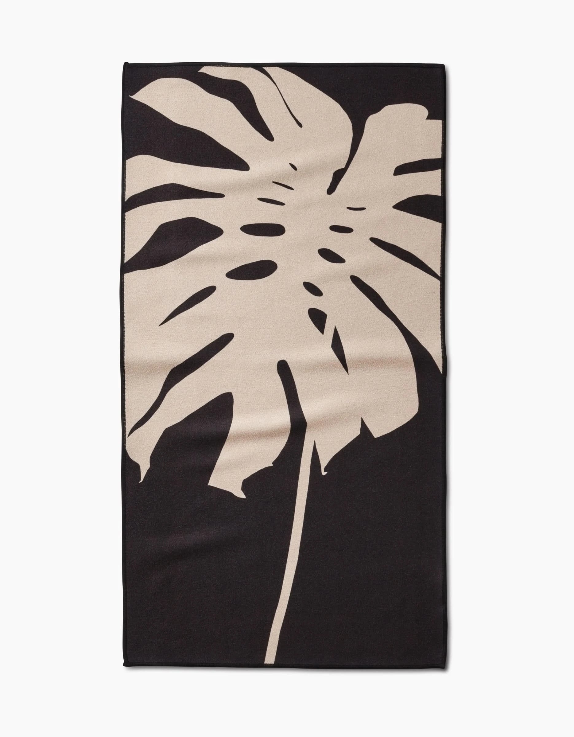 The PrintedPlant Cream Monstera Fitness Towel is rectangular, made from ultra-absorbent recycled materials, and features a large light beige monstera leaf design on a solid black background.