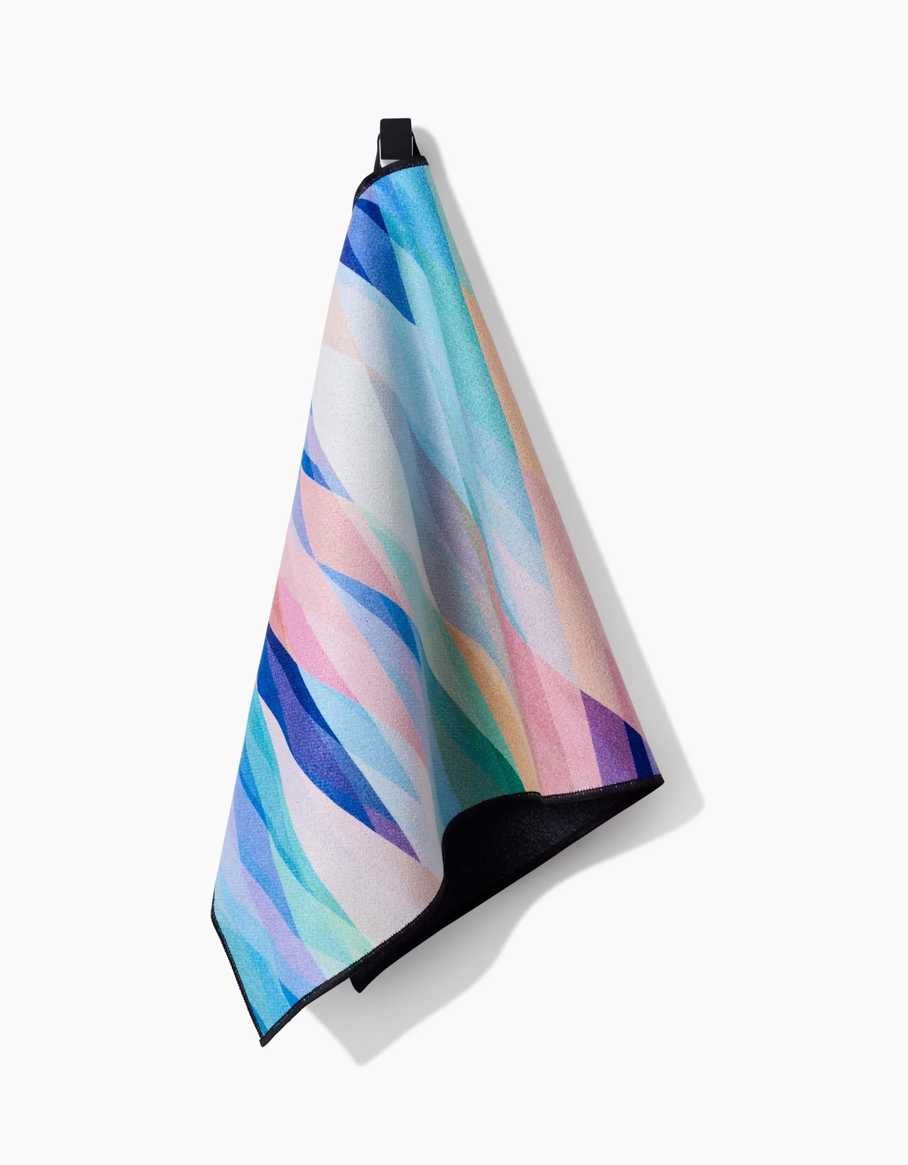 The Eventide towel by Rachel Parker, featuring a vibrant abstract wavy pattern in blues, pinks, purples, and yellows, hangs on a black hook against a white background.