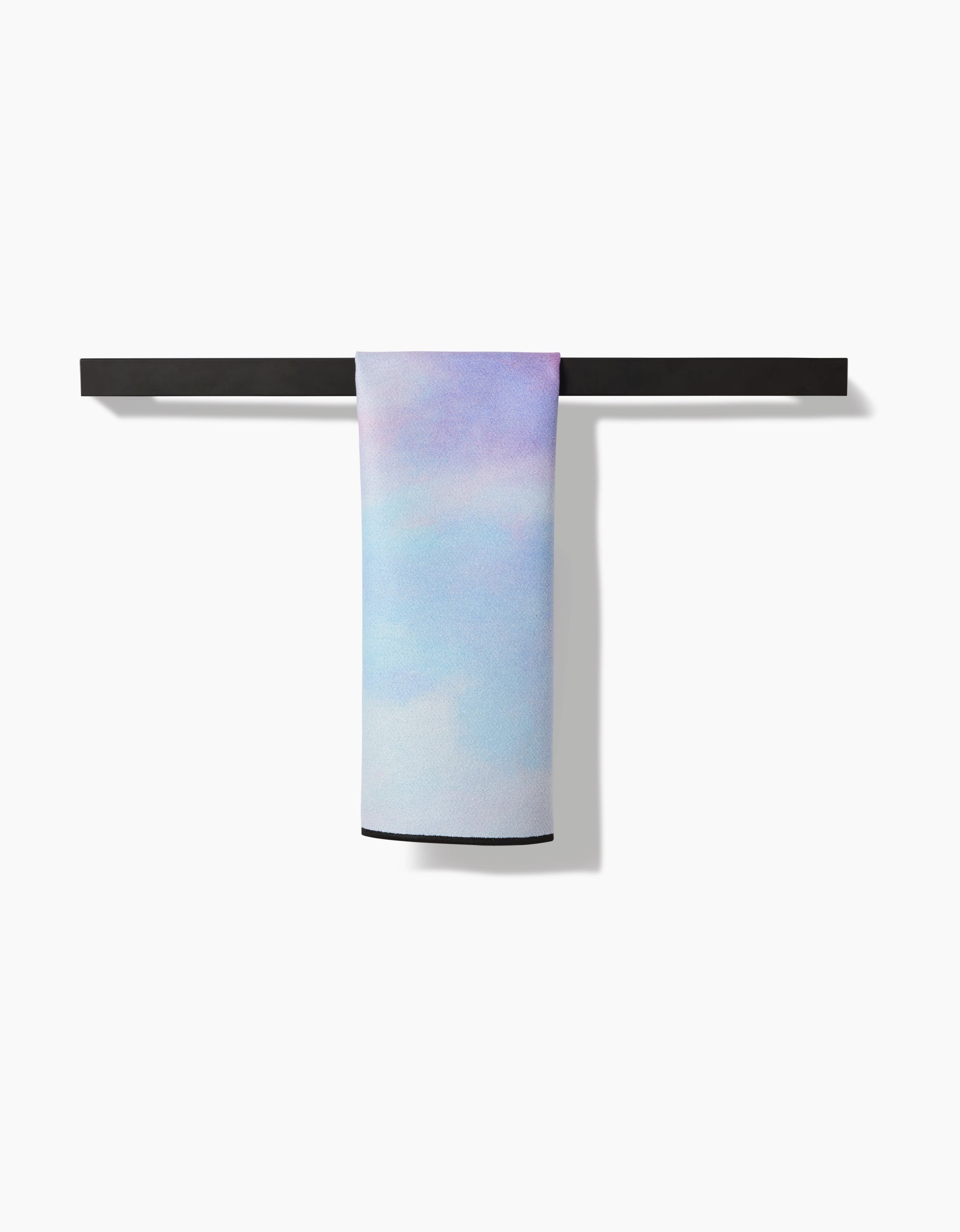 The Stefanie Bales Magic In The Sky pastel towel, with blue, pink, and purple hues, hangs neatly on a sleek black towel bar against a plain white background.